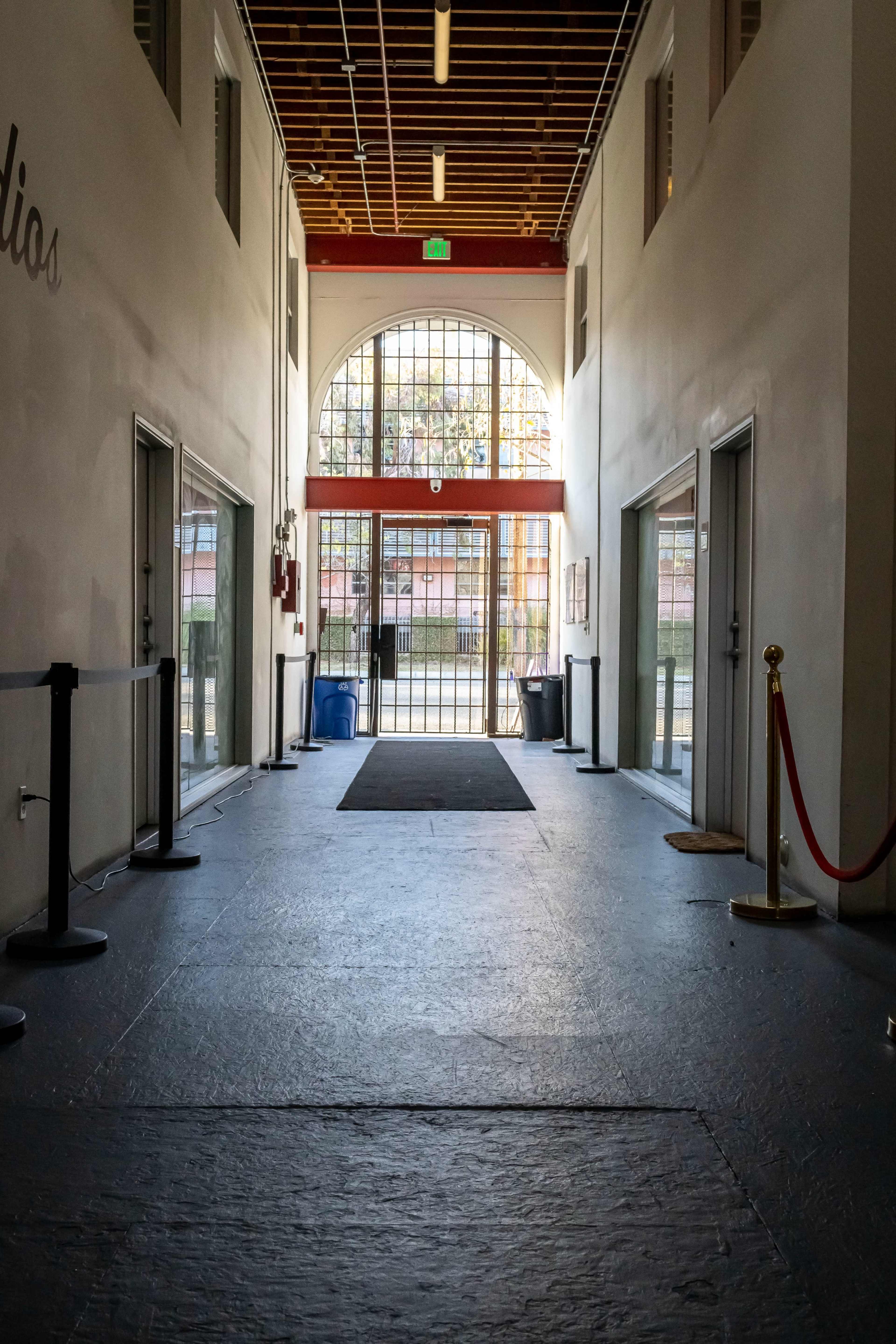 A long, empty hallway leading to a large arched window at the far end, with doors on either side and a red carpet runner in the center.
