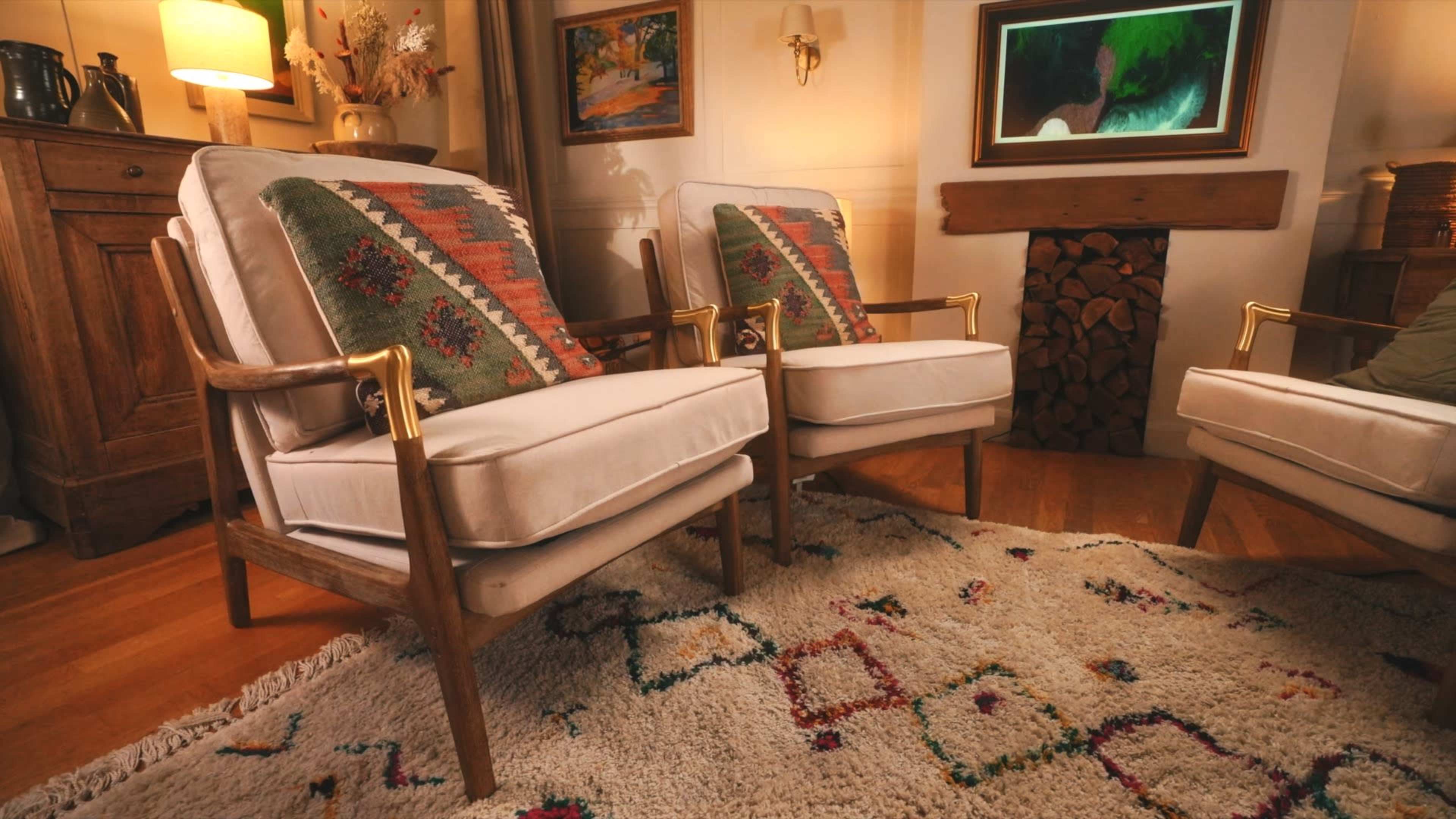The image shows two armchairs with patterned cushions facing a decorative fireplace, set in a cozy living room.