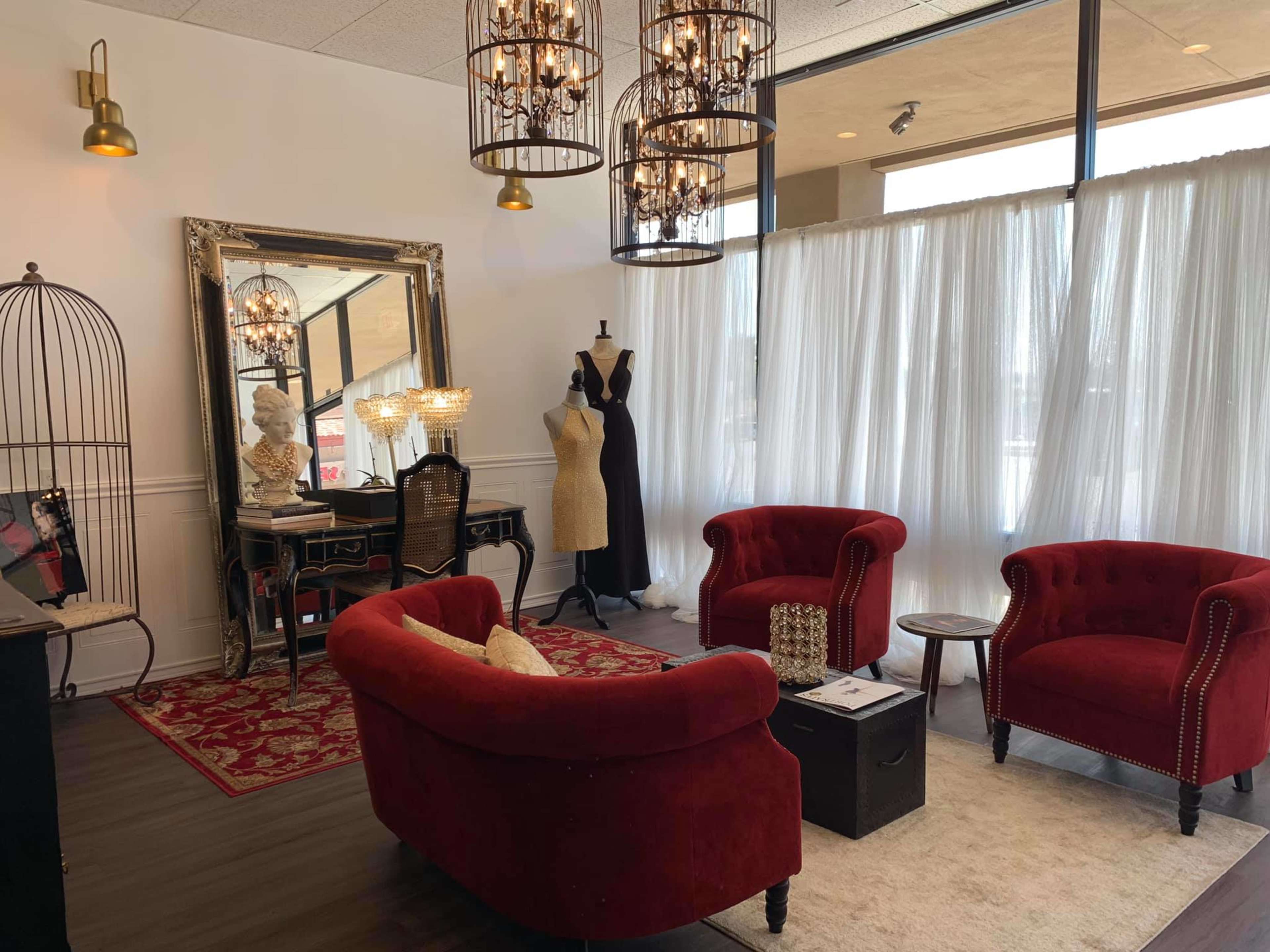 A stylish boutique interior featuring red velvet chairs, a mirror, a mannequin, a dressing table, and draped curtains.