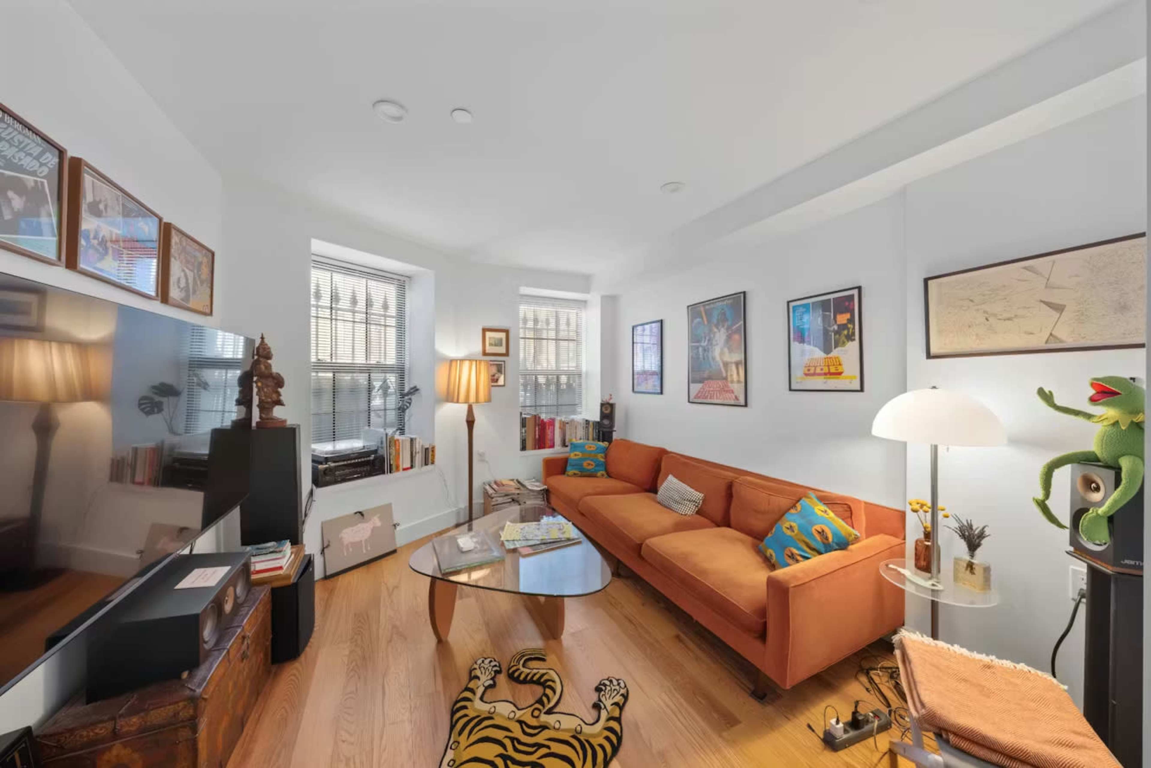 The room features a cozy living space with a brown sofa, a glass coffee table, and various decorative items, including framed art on the walls.