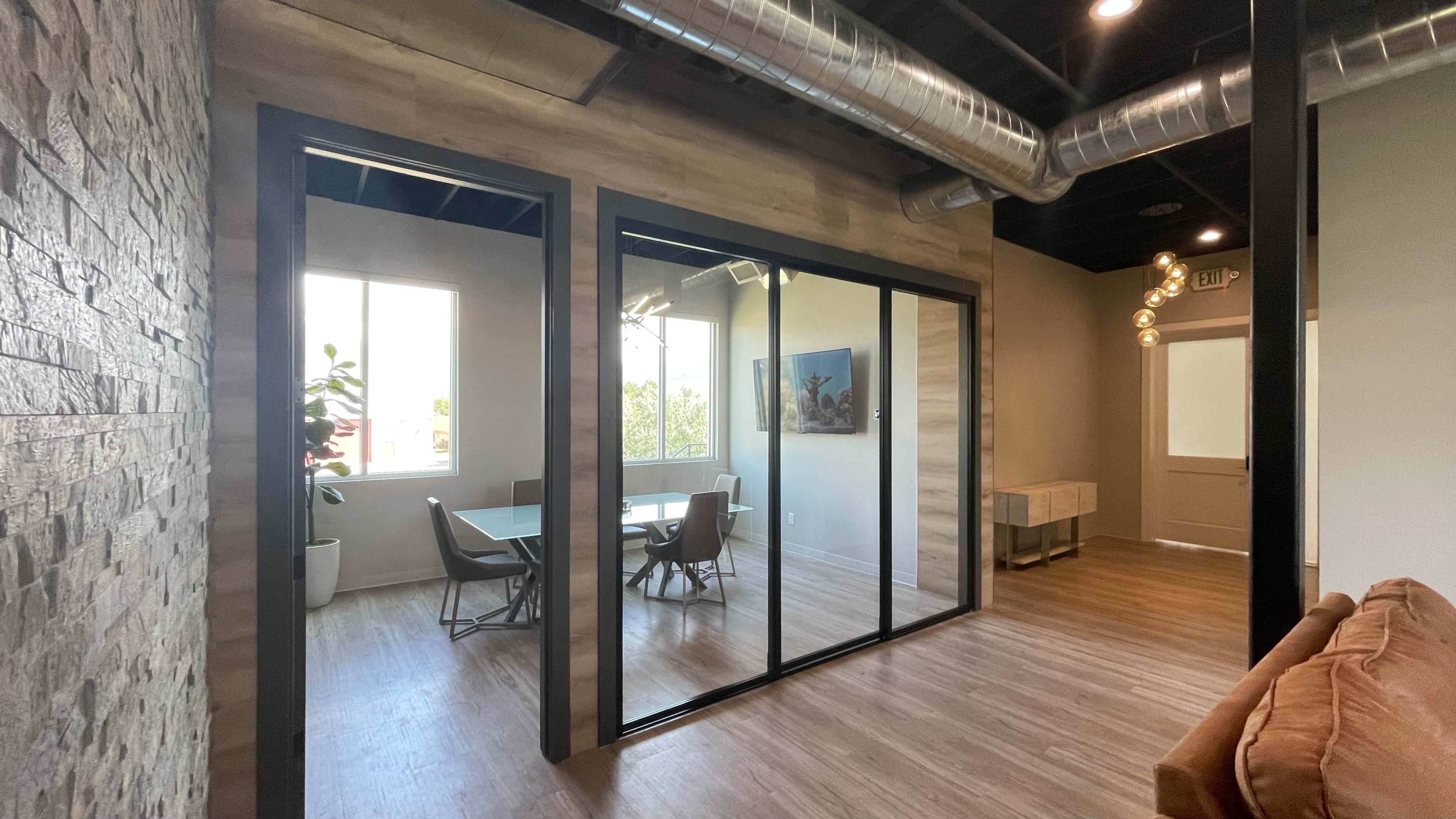 A modern office space featuring a glass-walled conference room with a table and chairs, separated from a lounge area with a couch.