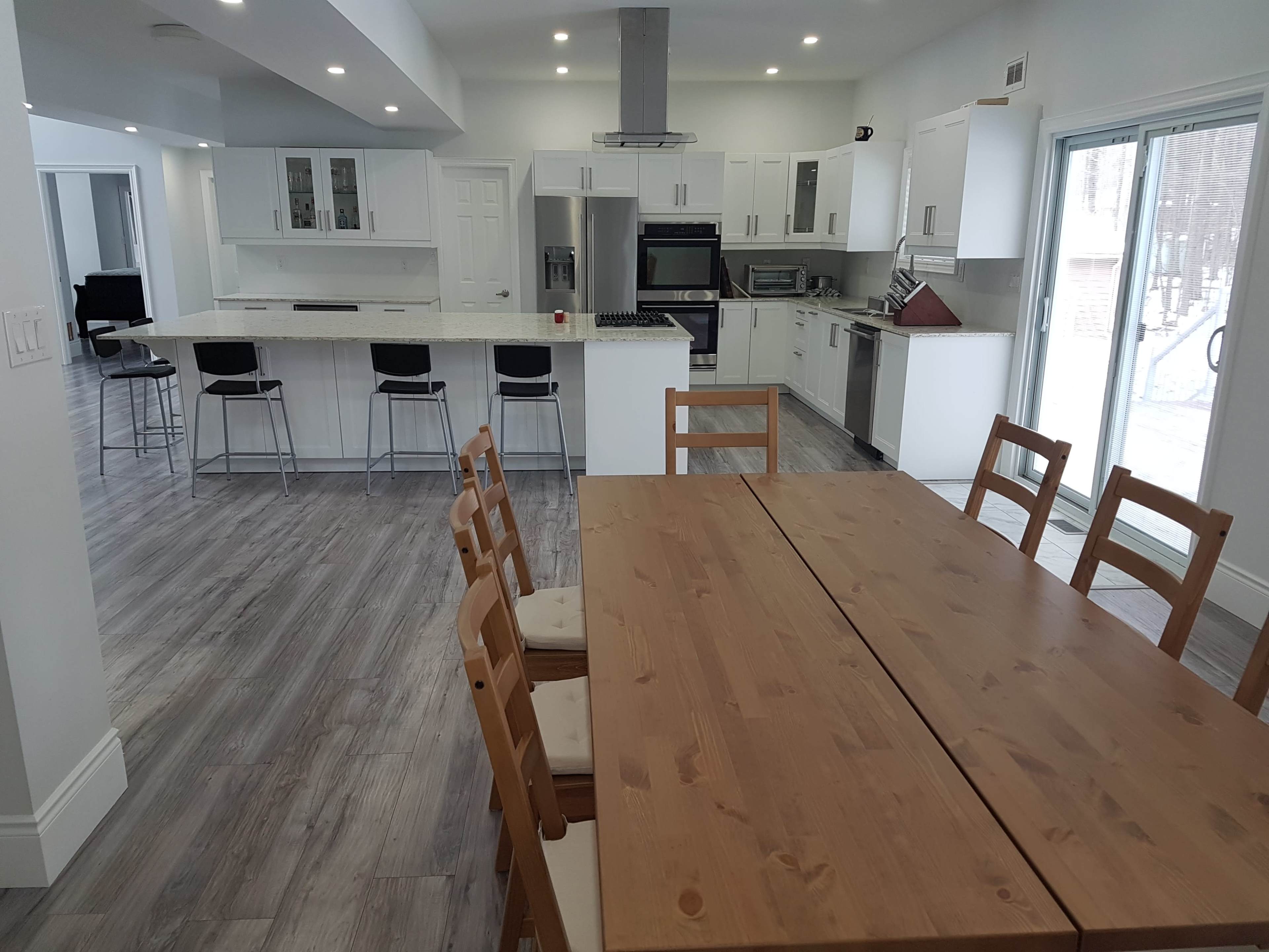 A spacious kitchen and dining area feature a large wooden table surrounded by chairs, with modern appliances and white cabinetry visible in the background.