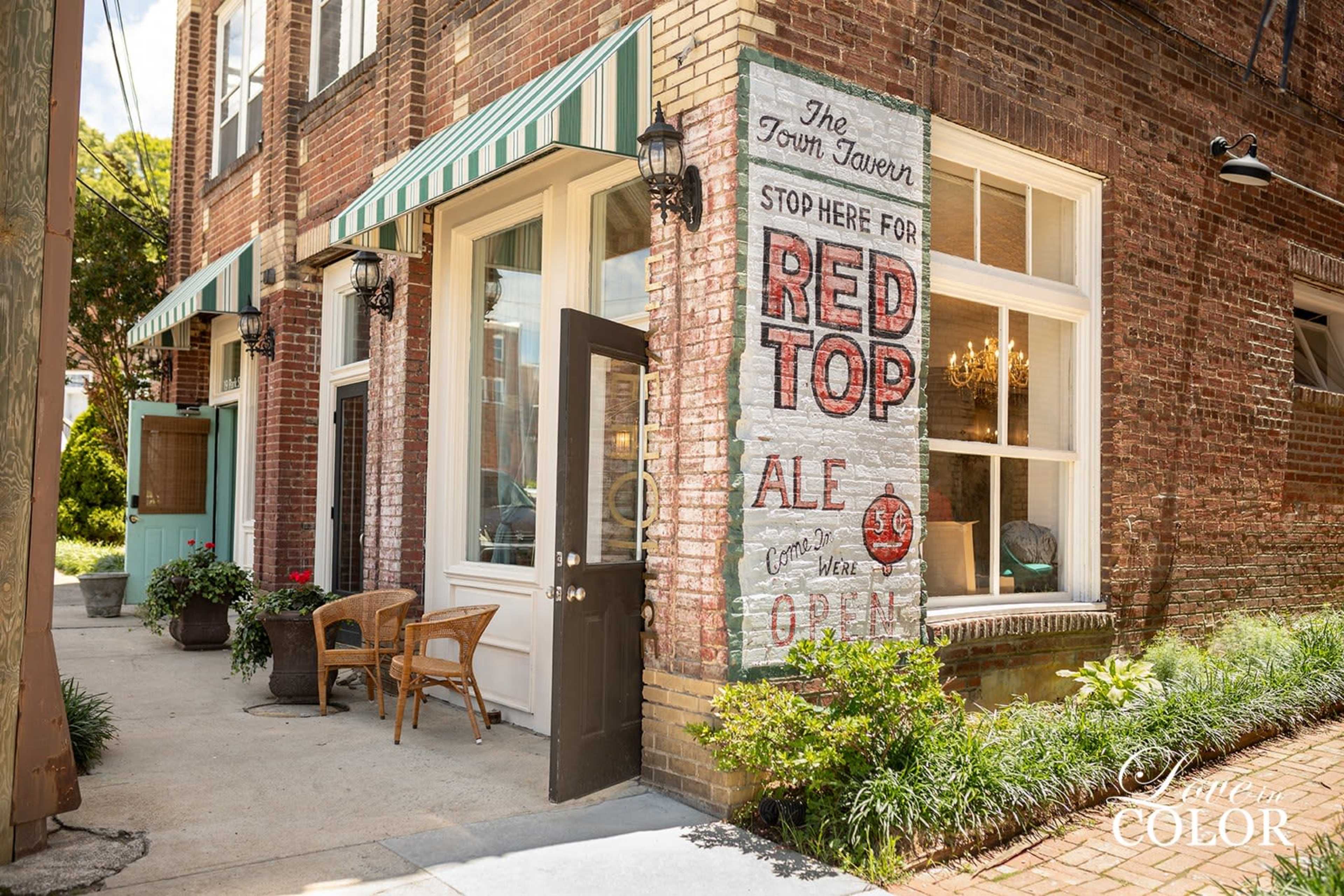 The exterior of a brick building with a painted sign advertising "Red Top Ale" and a door beneath a striped awning.