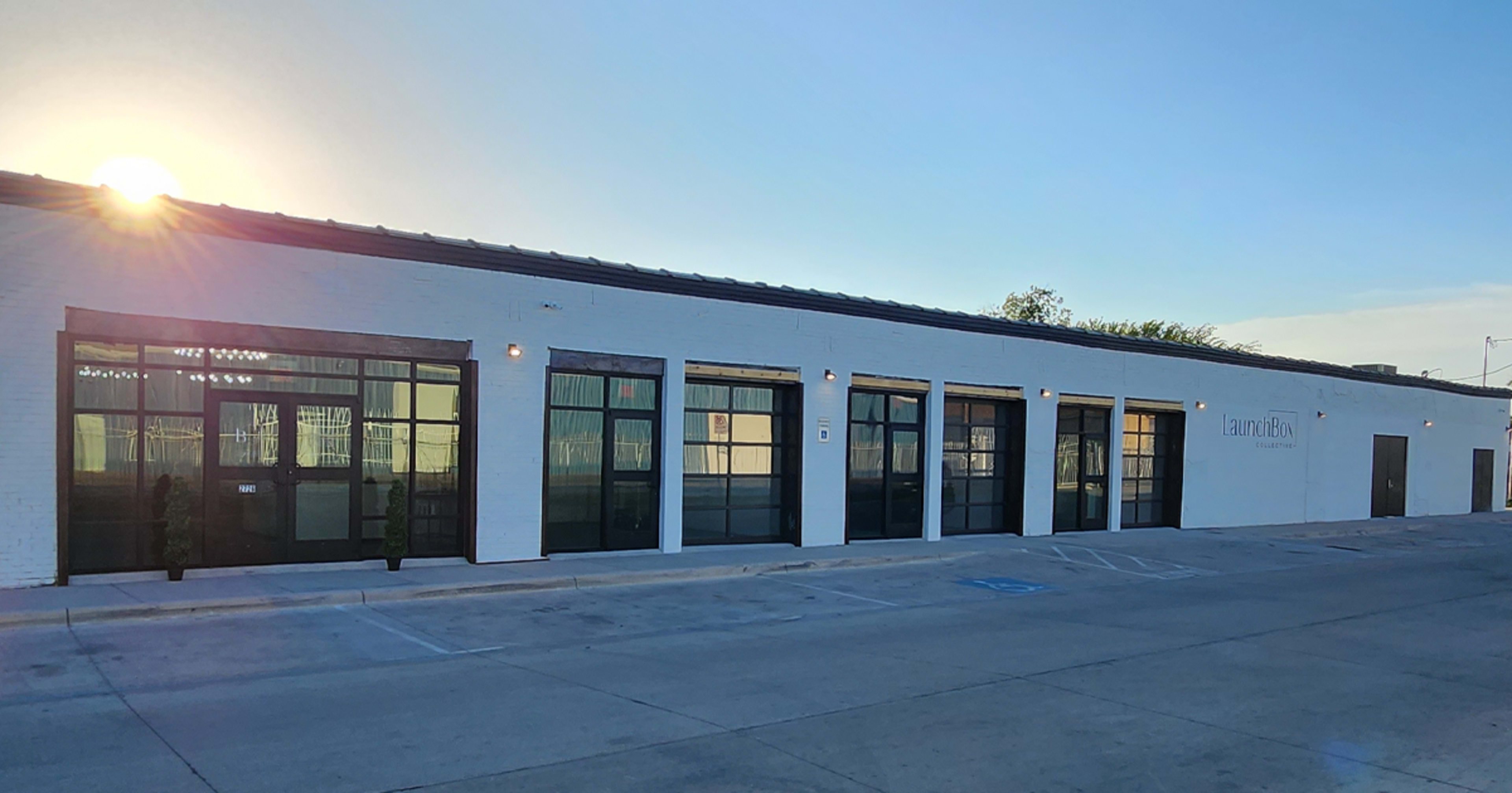 A modern, single-story building with large windows and a sleek, white exterior, set against a clear sky at sunset.
