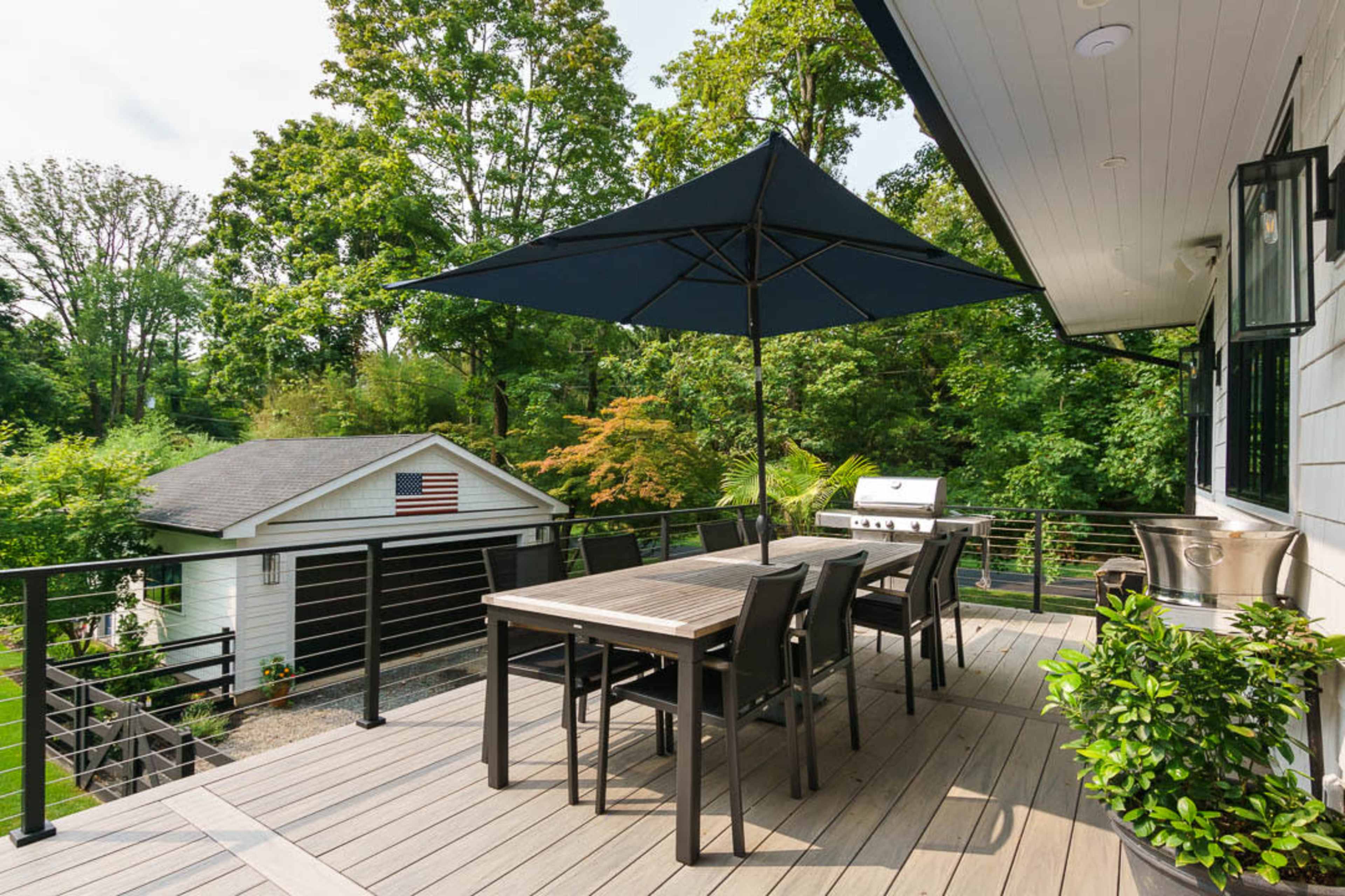 A deck with a large umbrella and dining set overlooks a yard with a garage featuring an American flag.