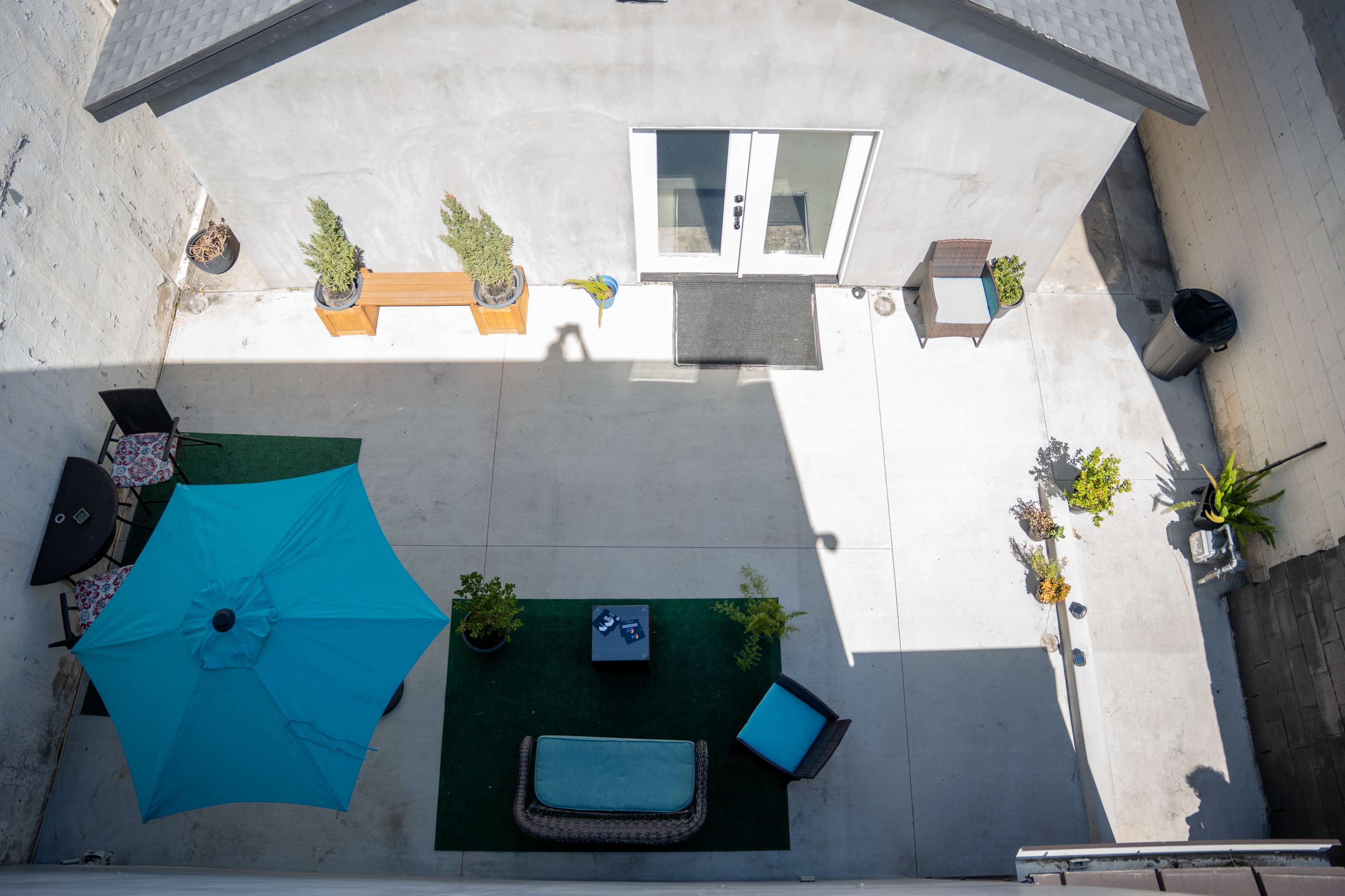 The image shows a small outdoor patio area with decorative plants, outdoor furniture, and an umbrella.