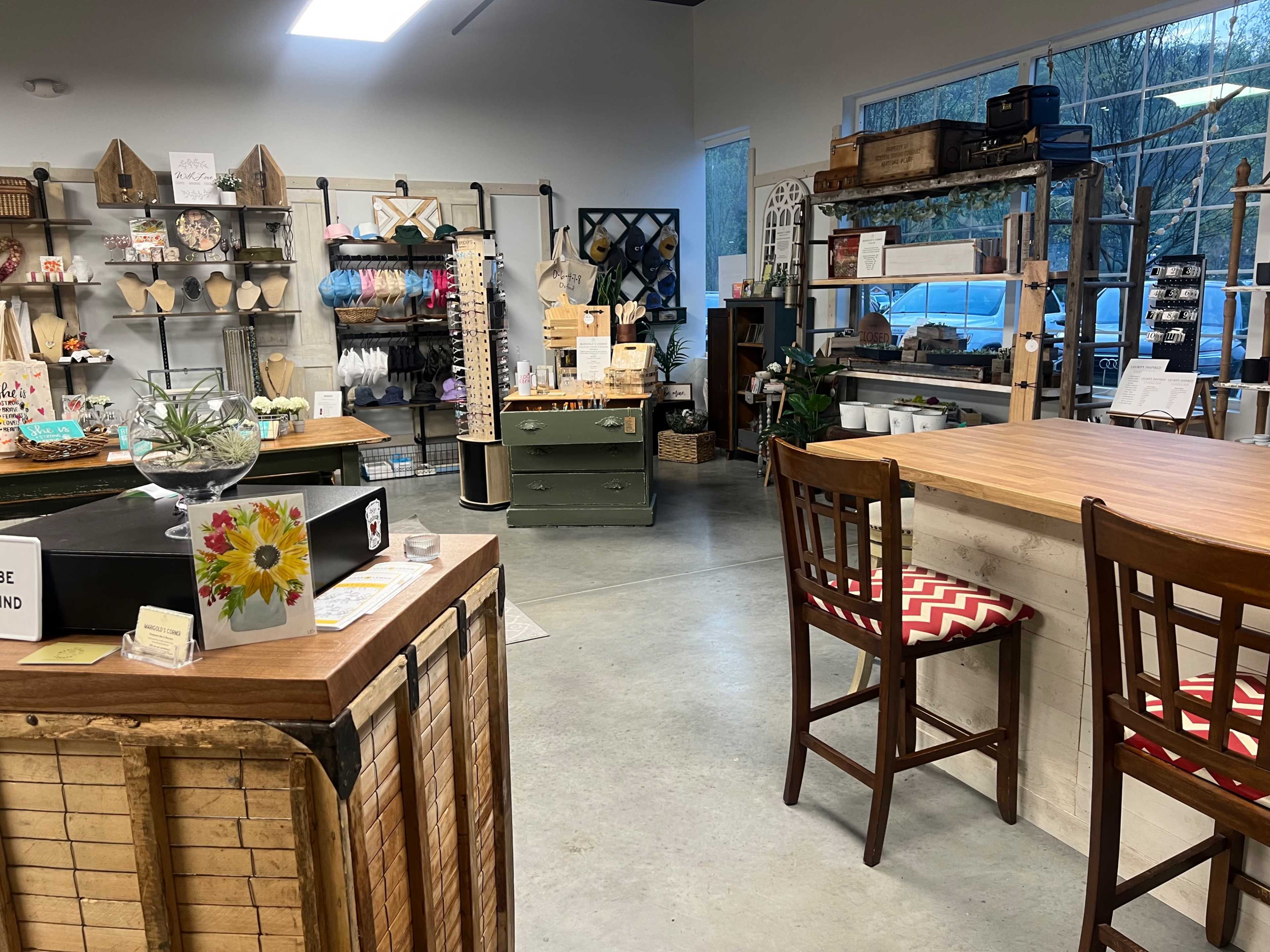 A bright retail space organized with various home decor items on display, wooden tables, and chairs for seating.