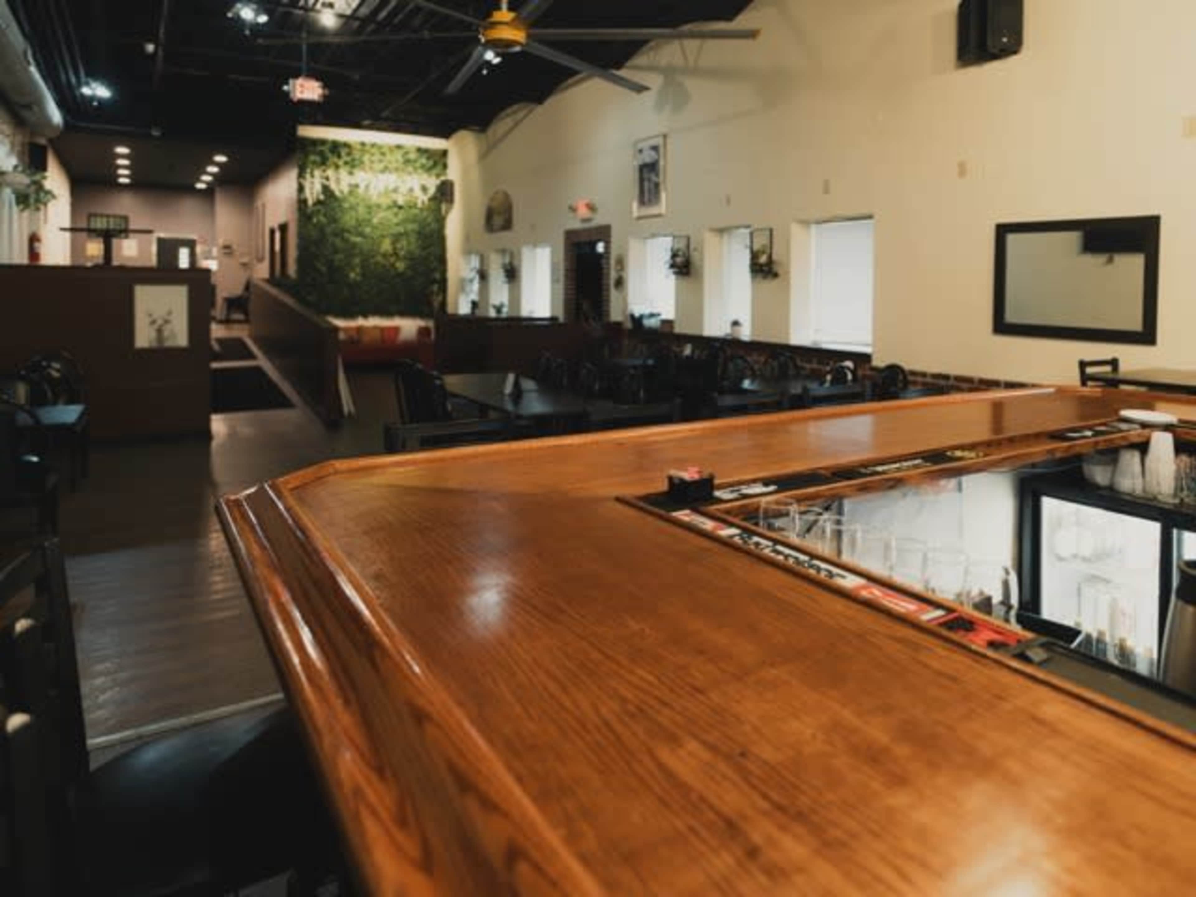 The image shows the interior of a restaurant with a wooden bar in the foreground and a dining area visible in the background.