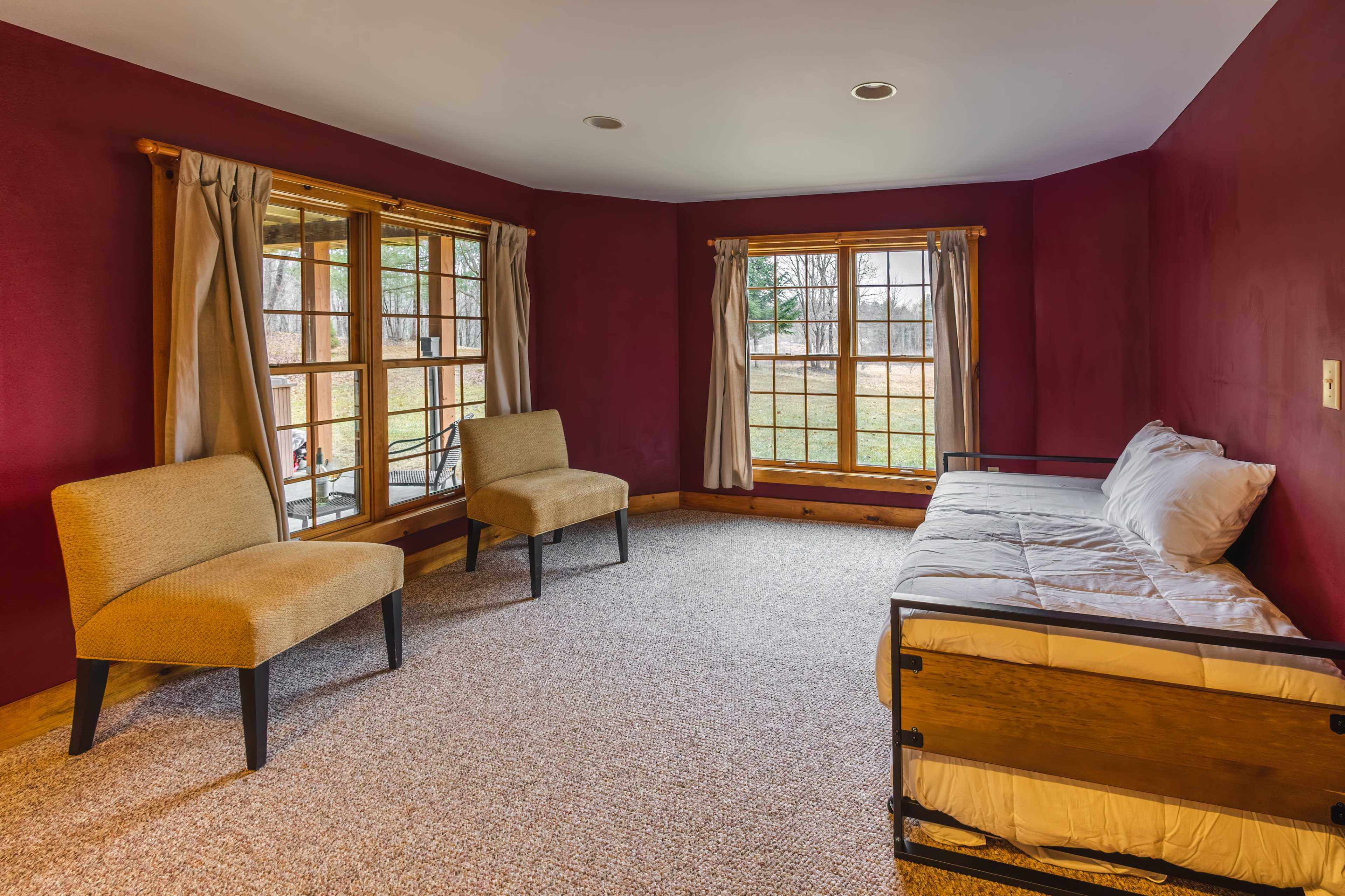 The room features two chairs and a daybed, with large windows that allow natural light to fill the space.