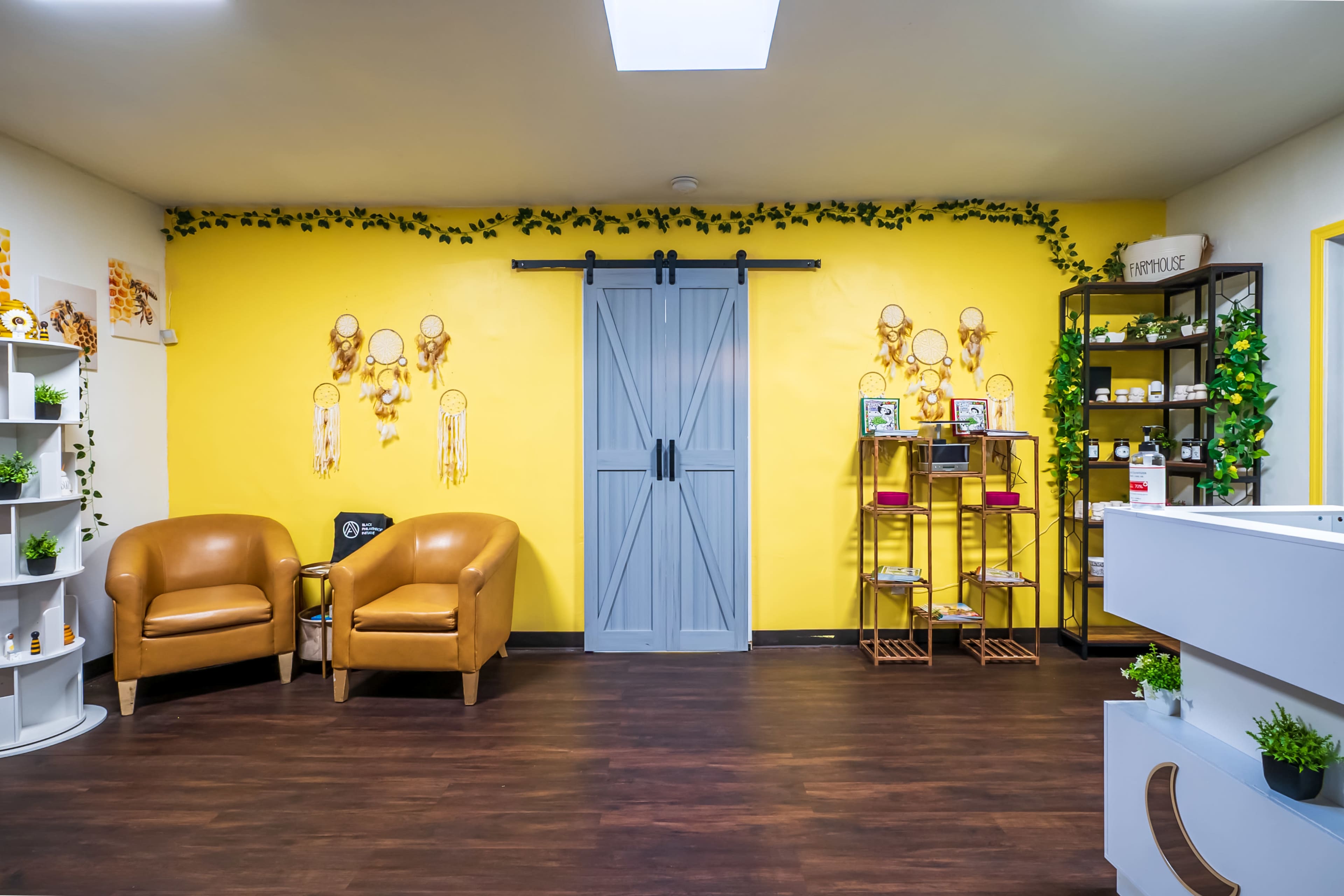 The image shows a bright room with yellow walls, featuring two brown armchairs, a sliding gray door, shelves with various items, and decorative plants.
