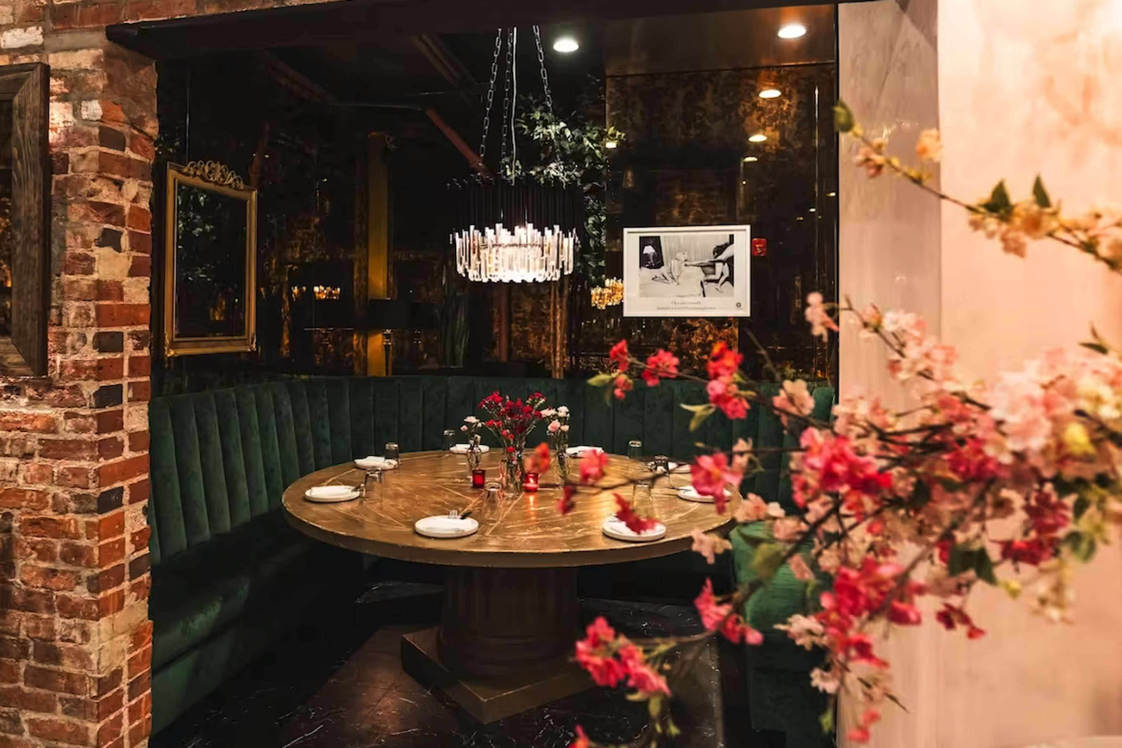 The image depicts a cozy dining area with a round wooden table surrounded by green upholstered seating, adorned with floral decorations and elegant lighting.