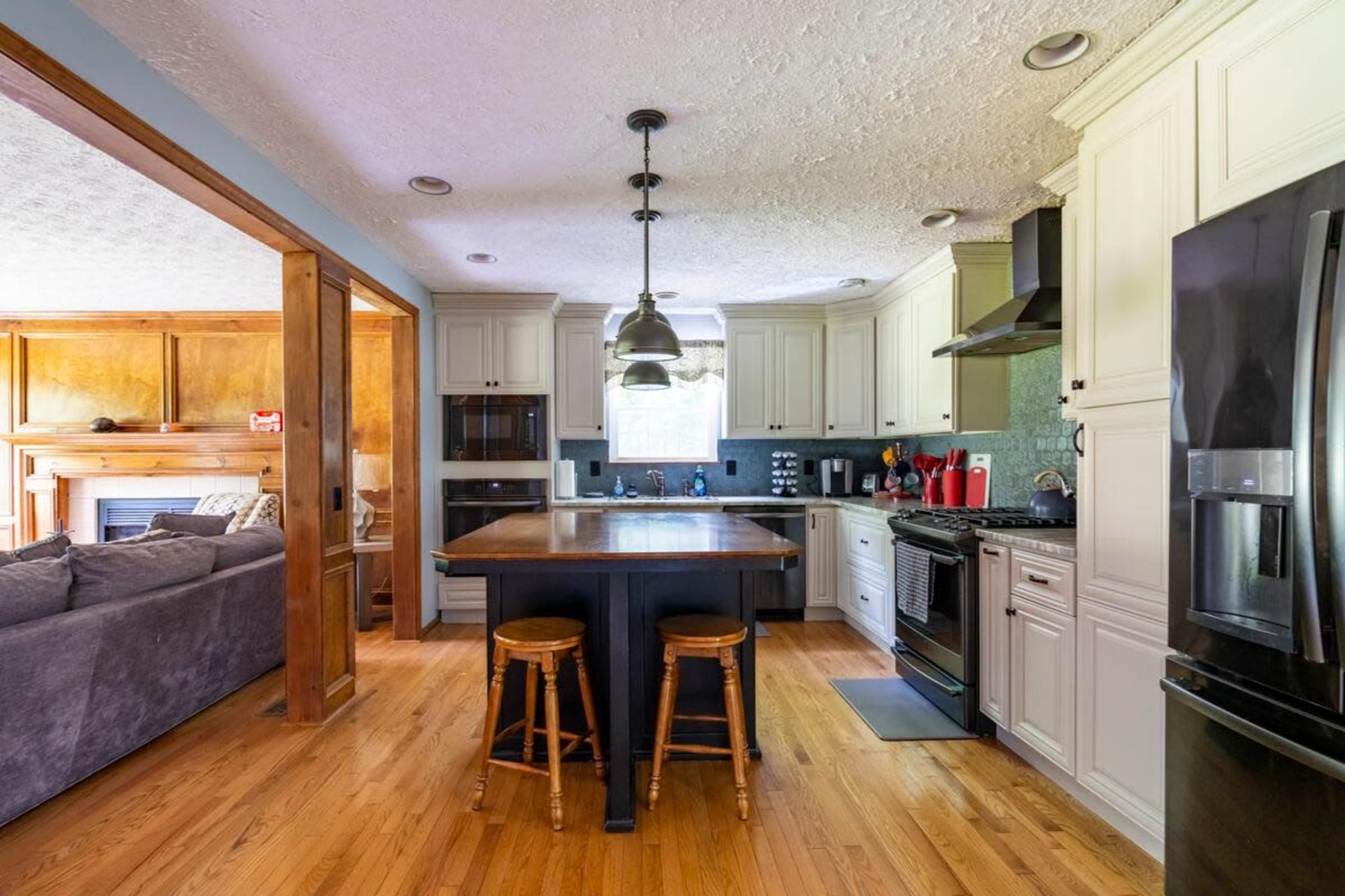 A modern kitchen features white cabinetry, a central island with two stools, and stainless steel appliances.