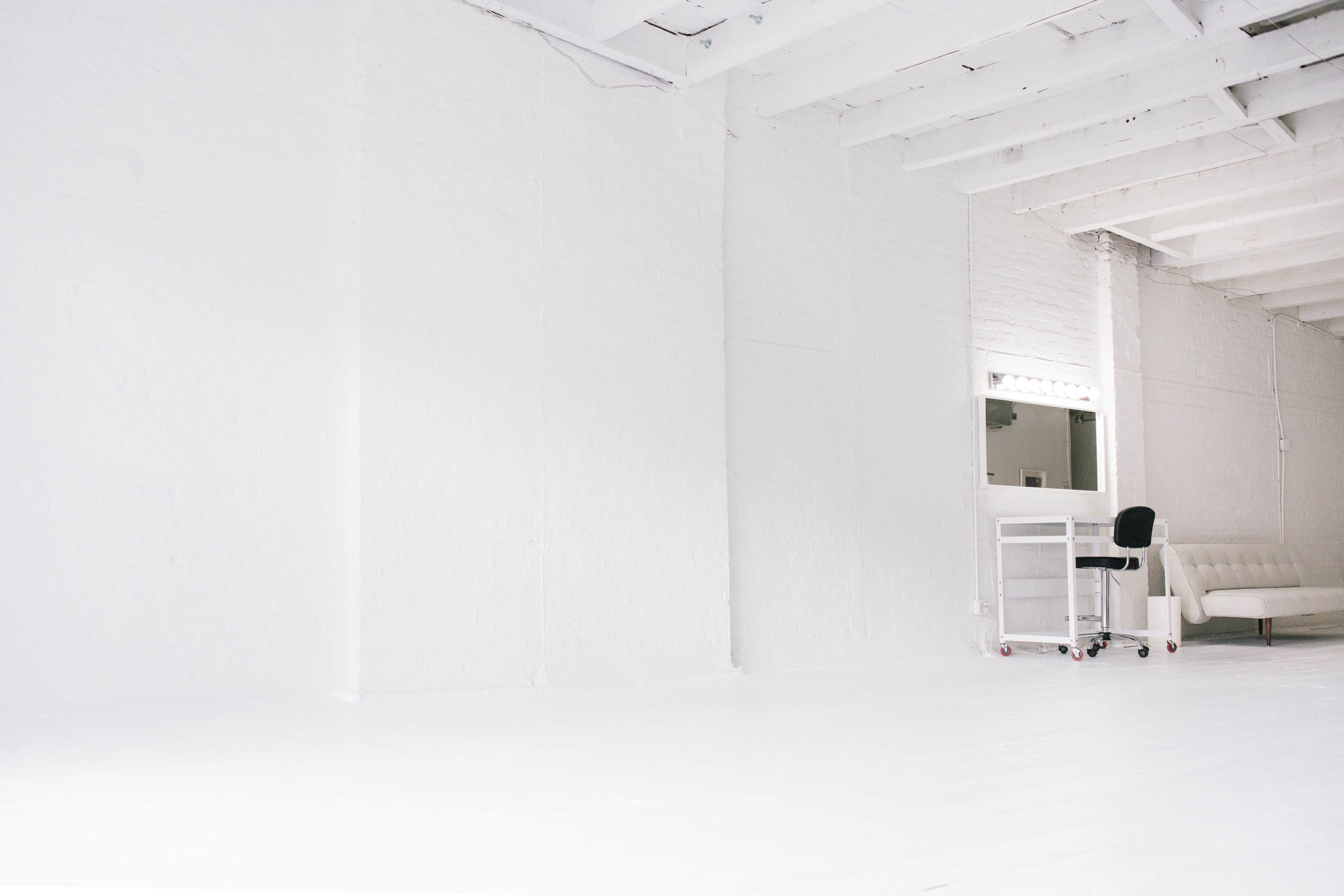 A bright, minimalistic room features white walls, a white floor, a white cart on wheels, and a white couch.