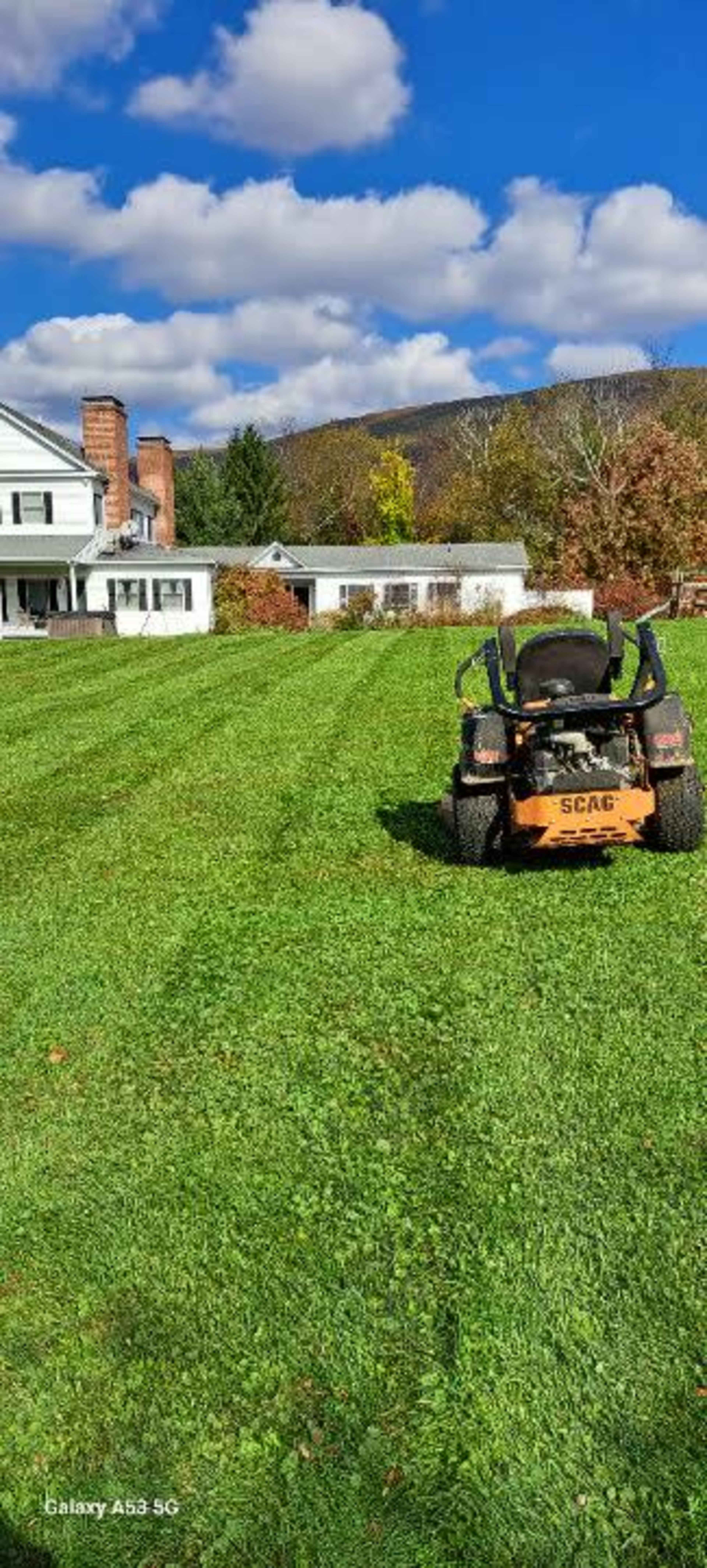 A riding lawn mower is parked on a well-manicured green lawn next to a house, with trees and a cloudy sky in the background.