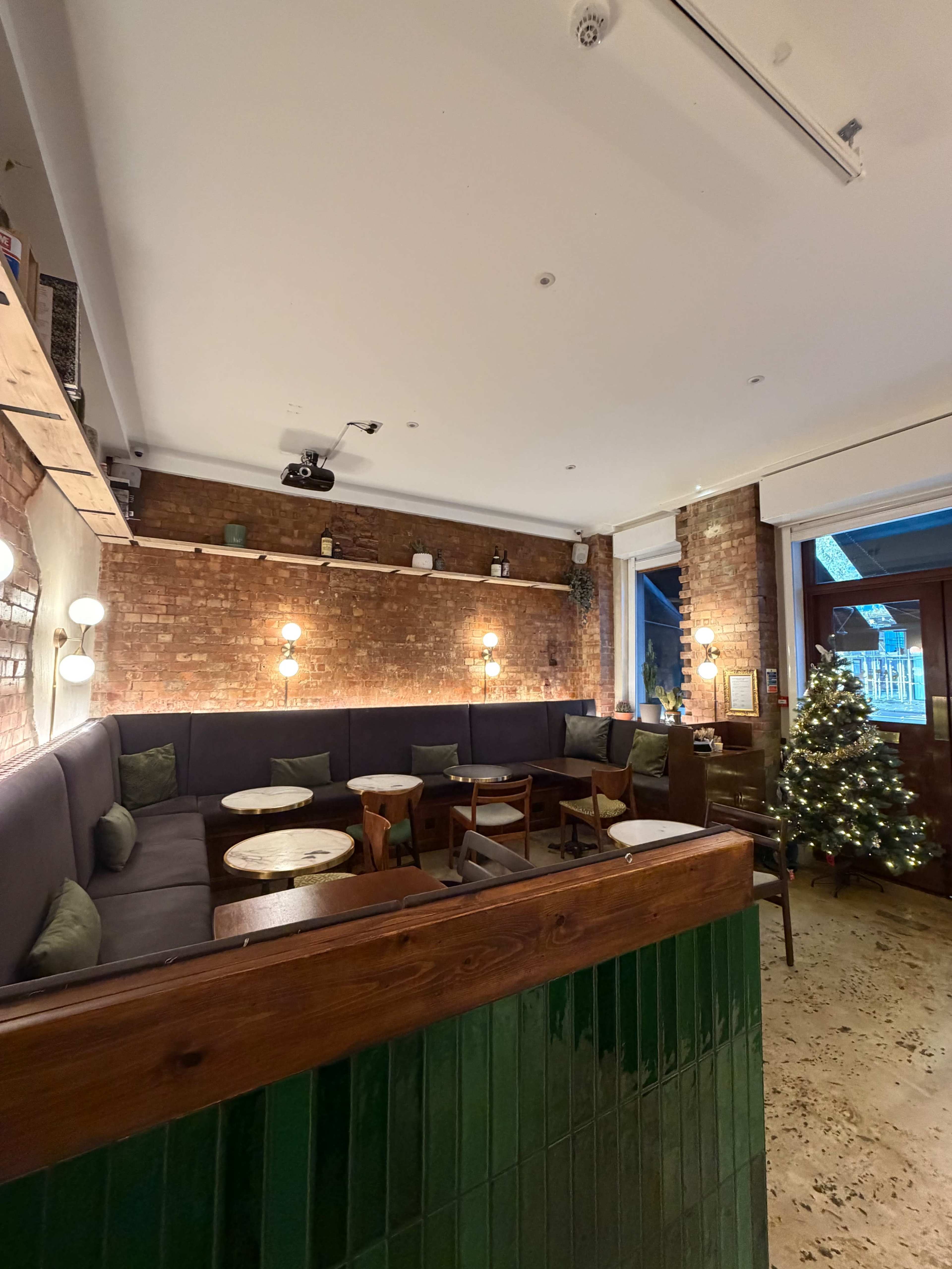 The image shows a cozy café interior with brick walls, wooden furniture, and a small decorated Christmas tree in the corner.