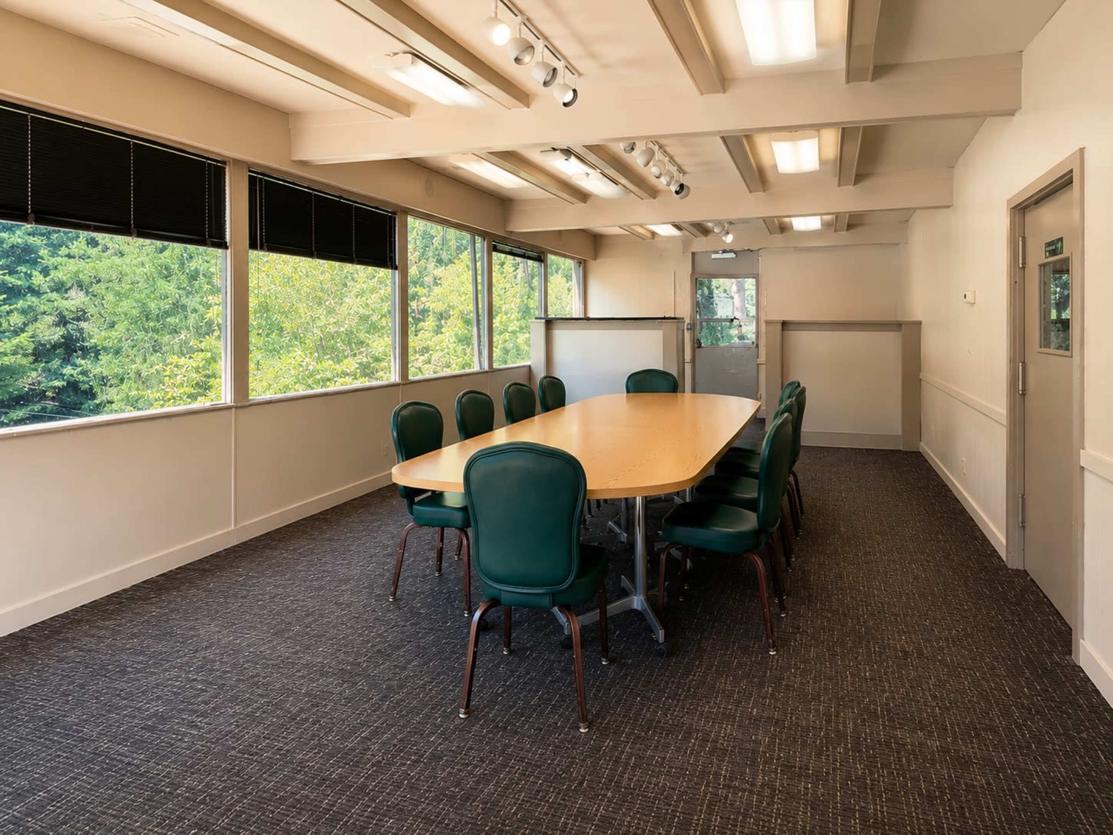 The image shows a conference room with a large oval table surrounded by green chairs, illuminated by natural light from windows.