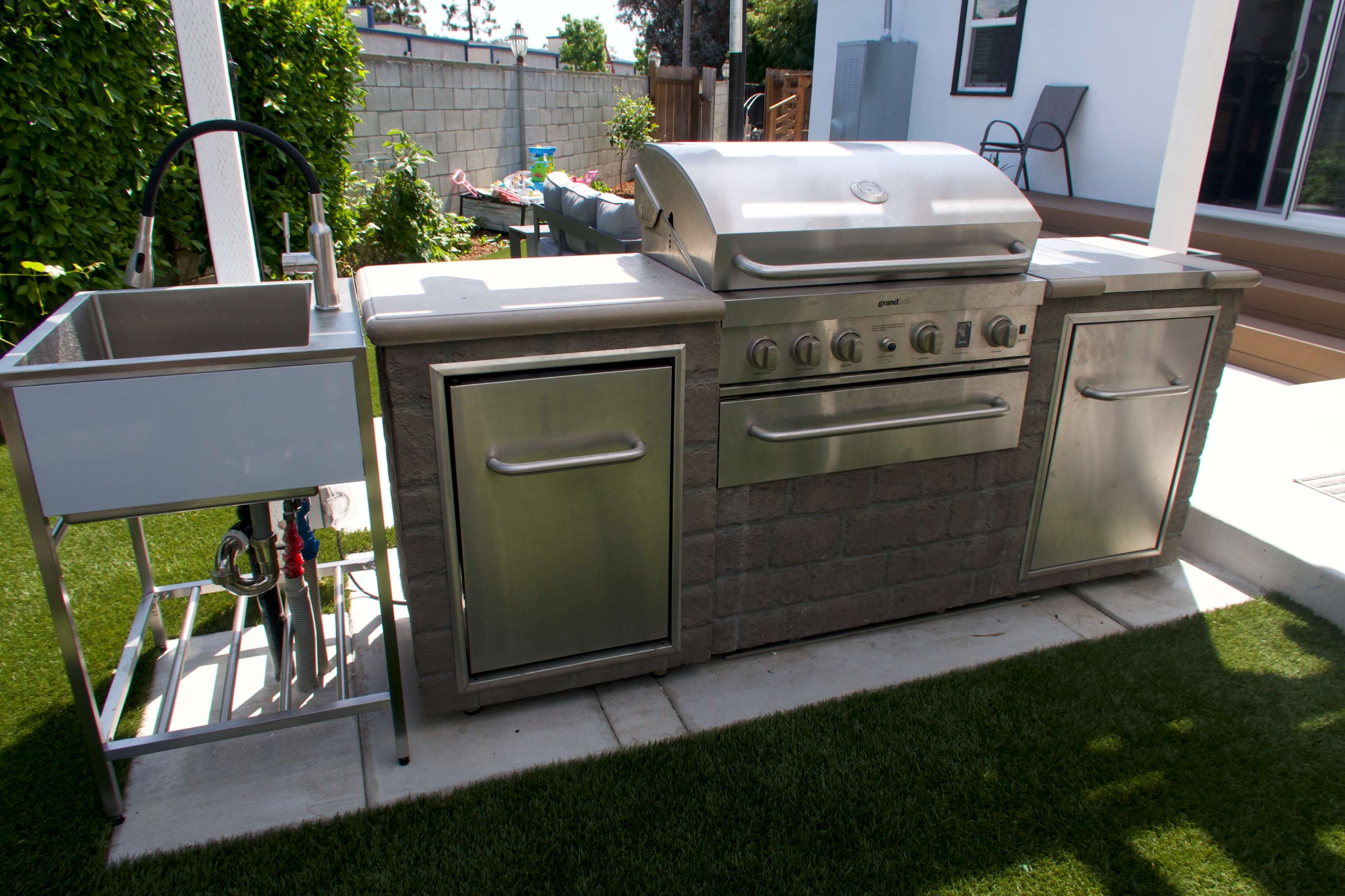 An outdoor kitchen with a stainless steel grill and a side sink on a concrete countertop.