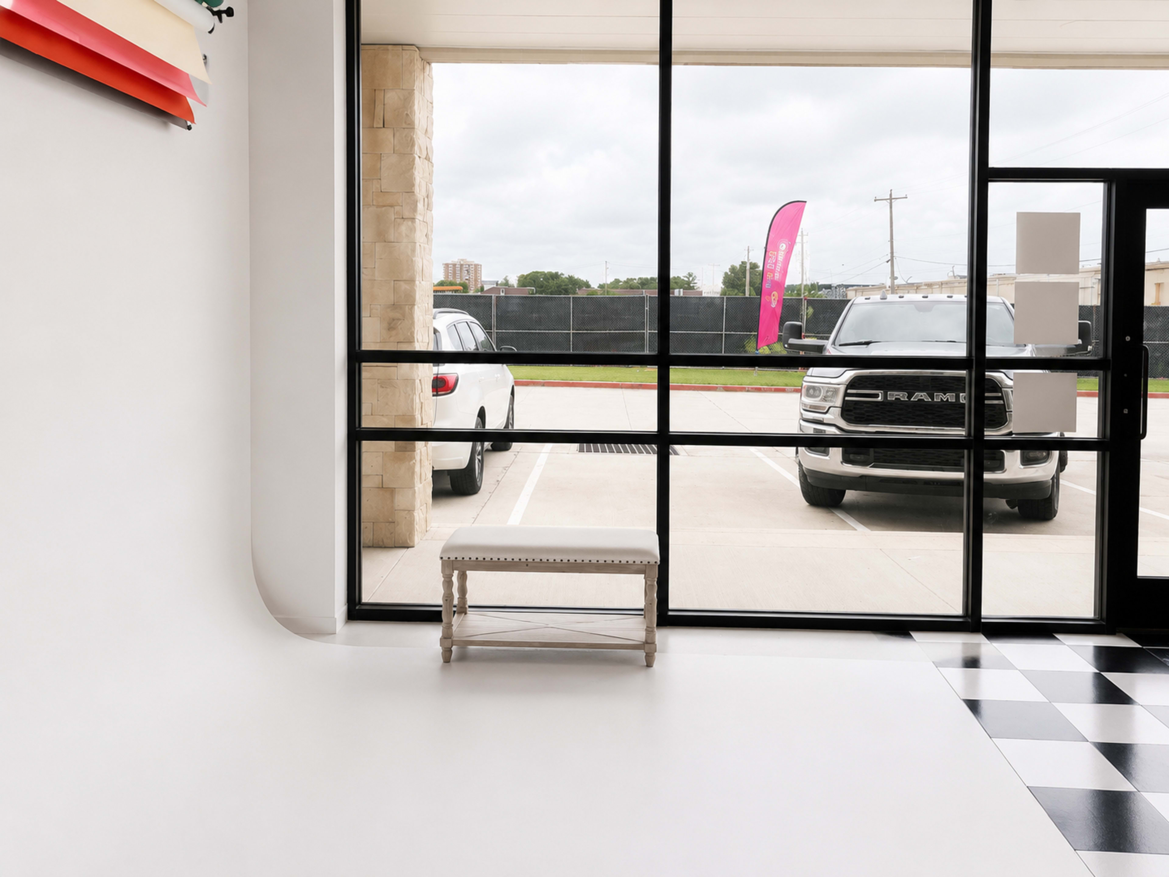 The image shows a spacious room with a window overlooking a parking lot, featuring a bench and a parked gray truck outside.