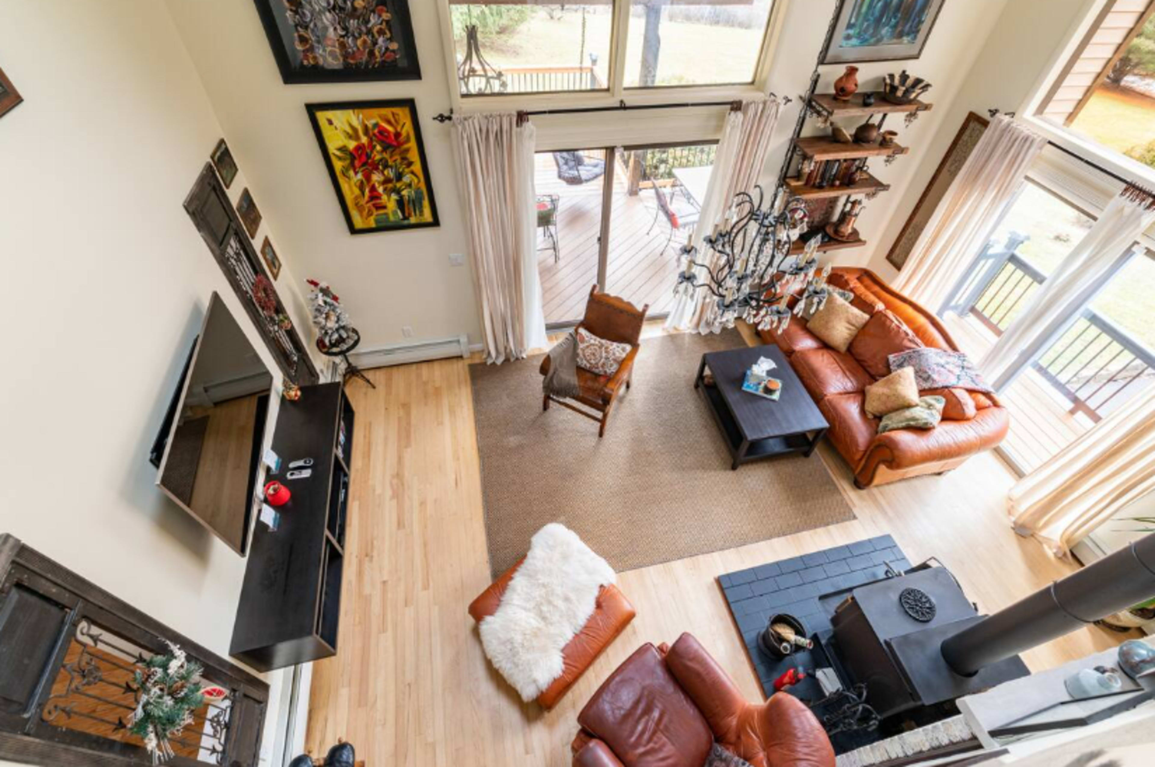 An open living room features large windows, wooden flooring, leather sofas, and a view of a deck outside.