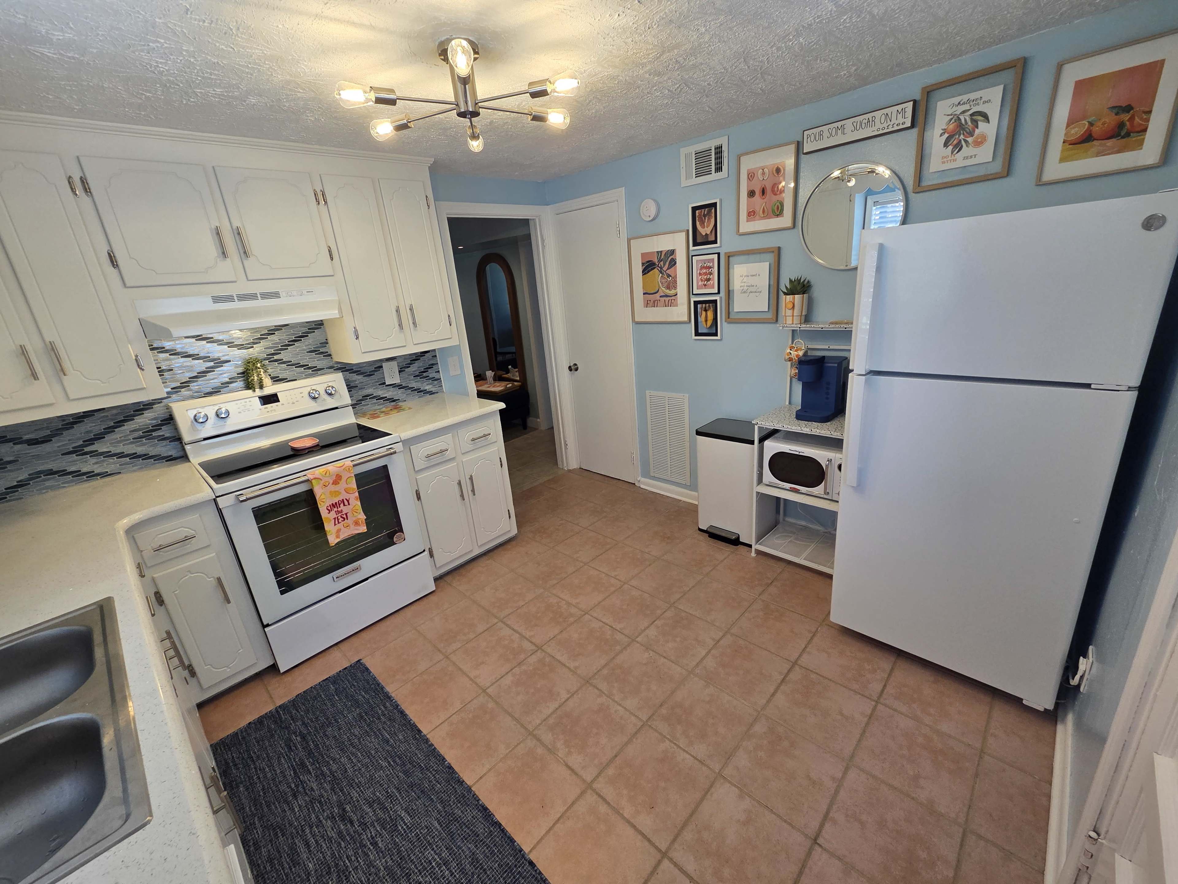 The image shows a tiled kitchen with white cabinets, modern appliances, and blue accents on the walls.