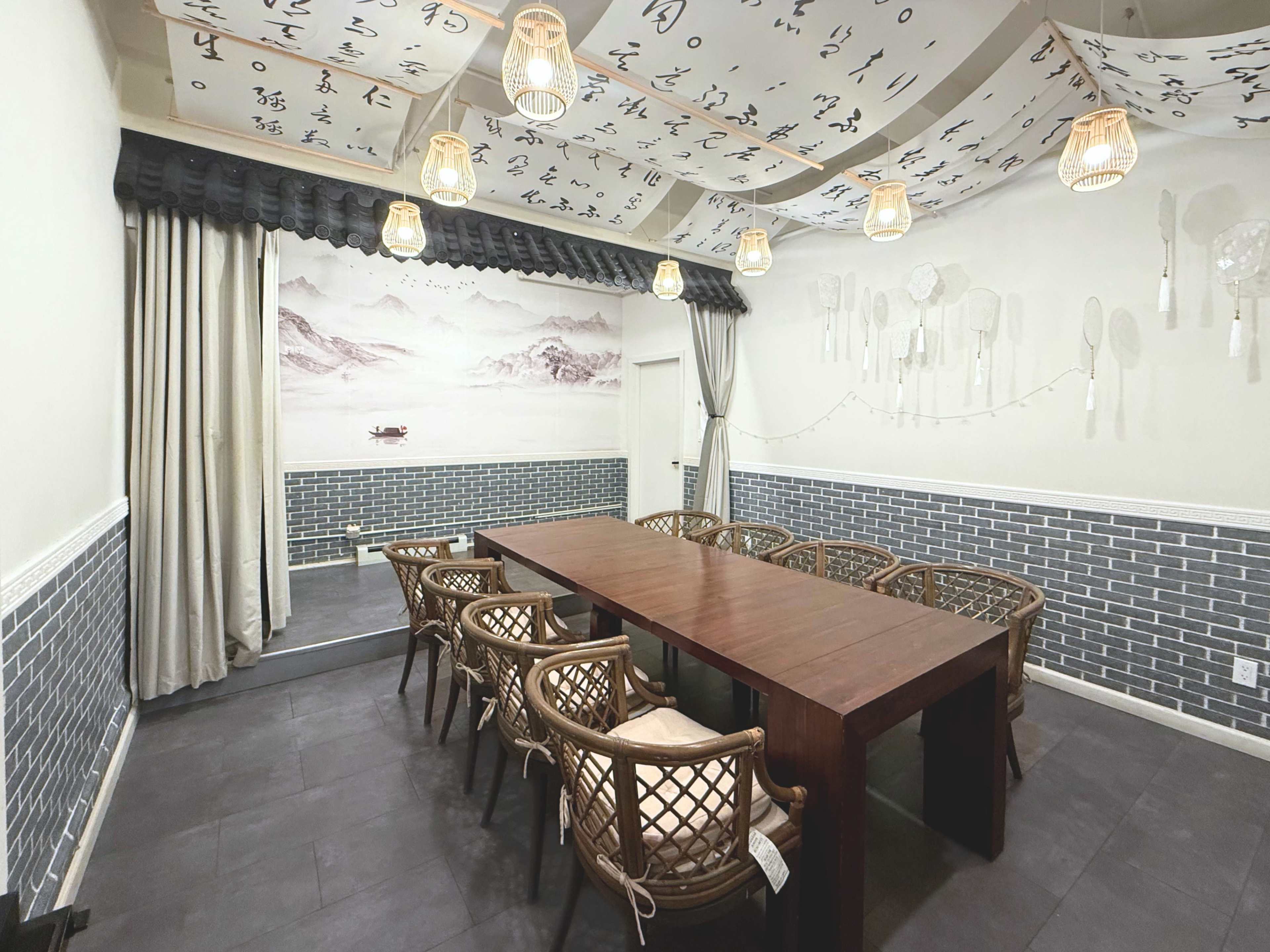 The image shows a dining room with a large wooden table surrounded by woven chairs, complemented by decorative ceiling features and wall art.