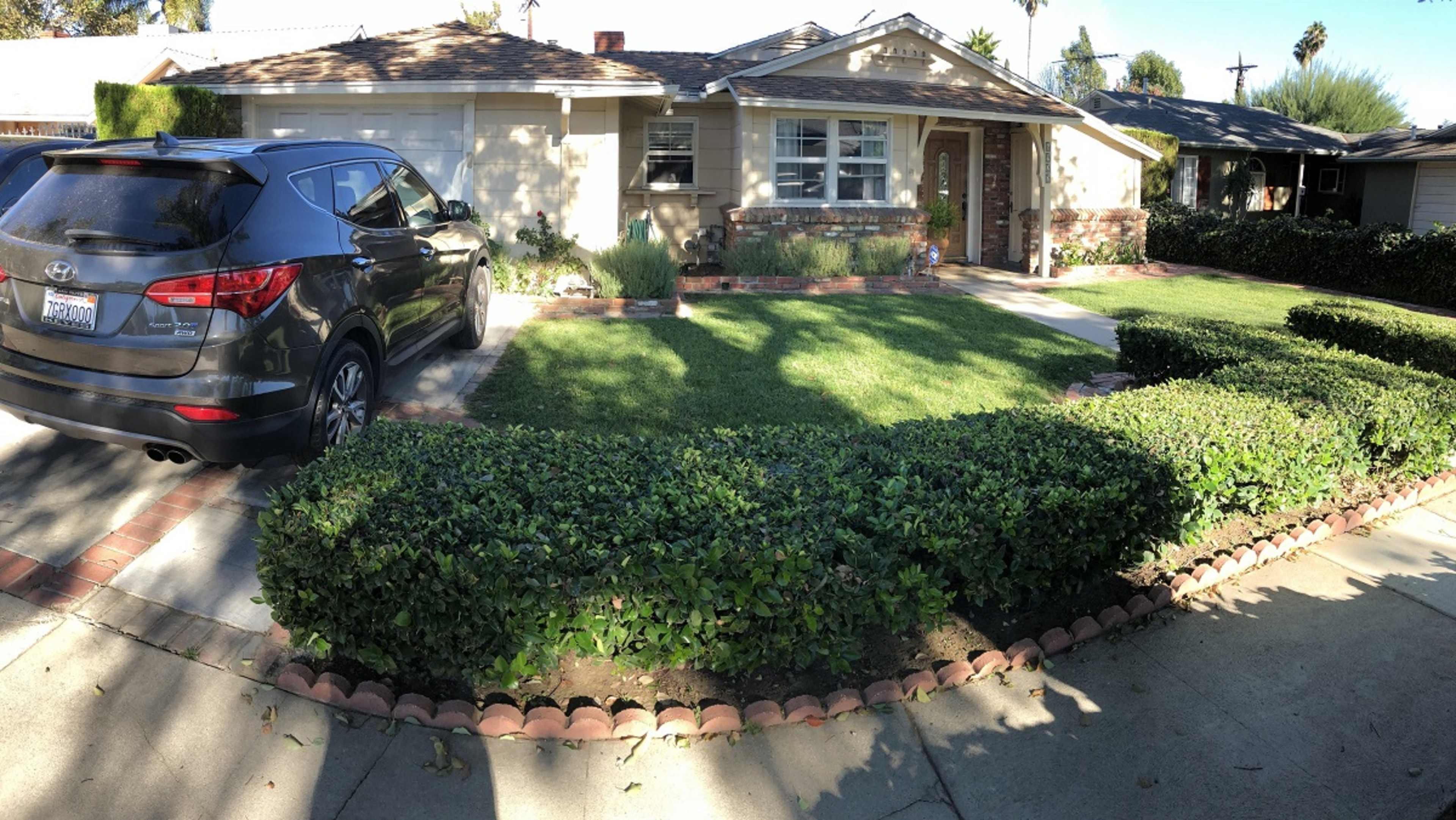 A black SUV is parked in the driveway of a single-story house with a neatly trimmed front lawn and hedges.