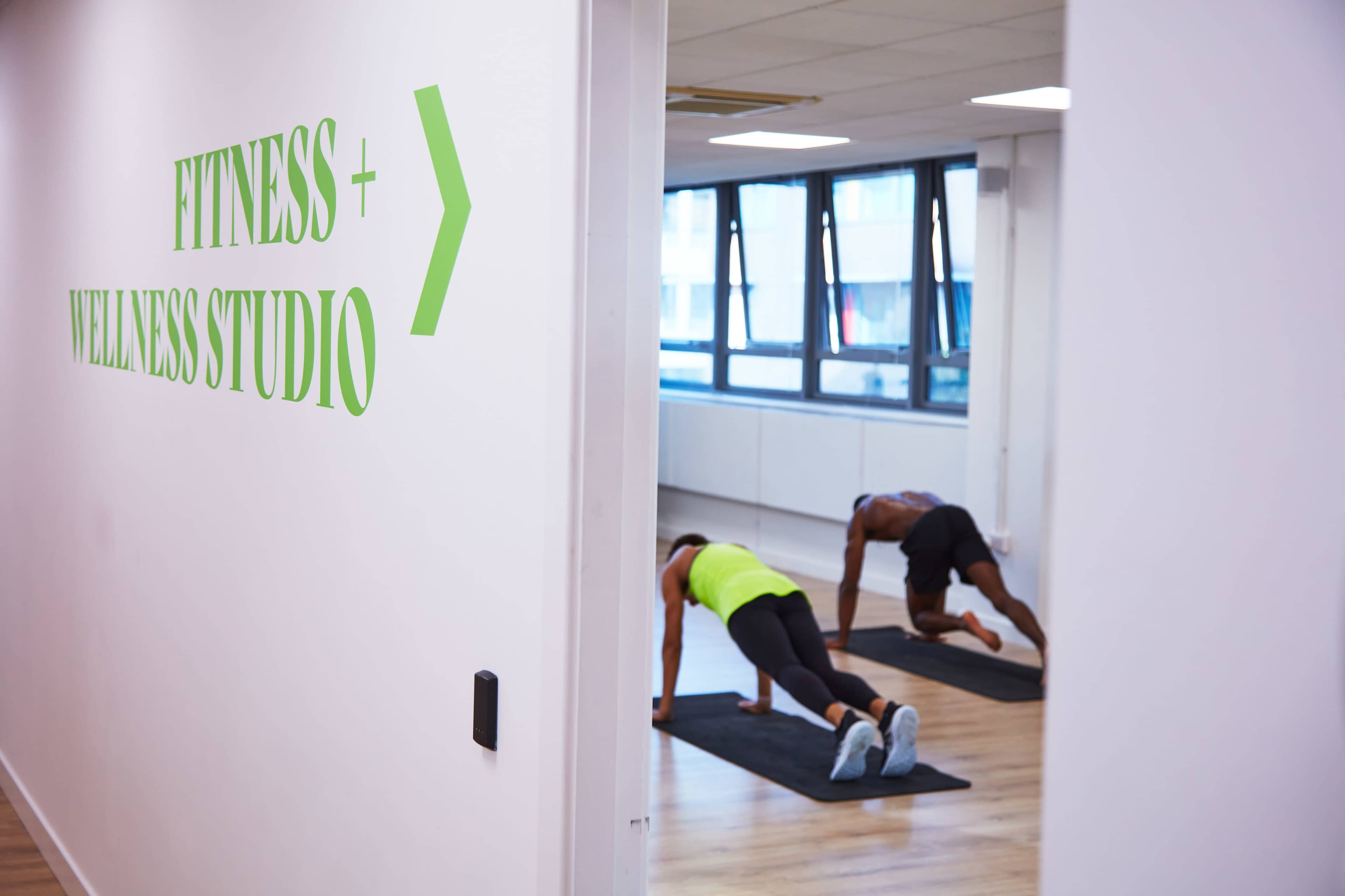 A fitness and wellness studio is visible through an open doorway, where two individuals are performing exercise routines on mats.