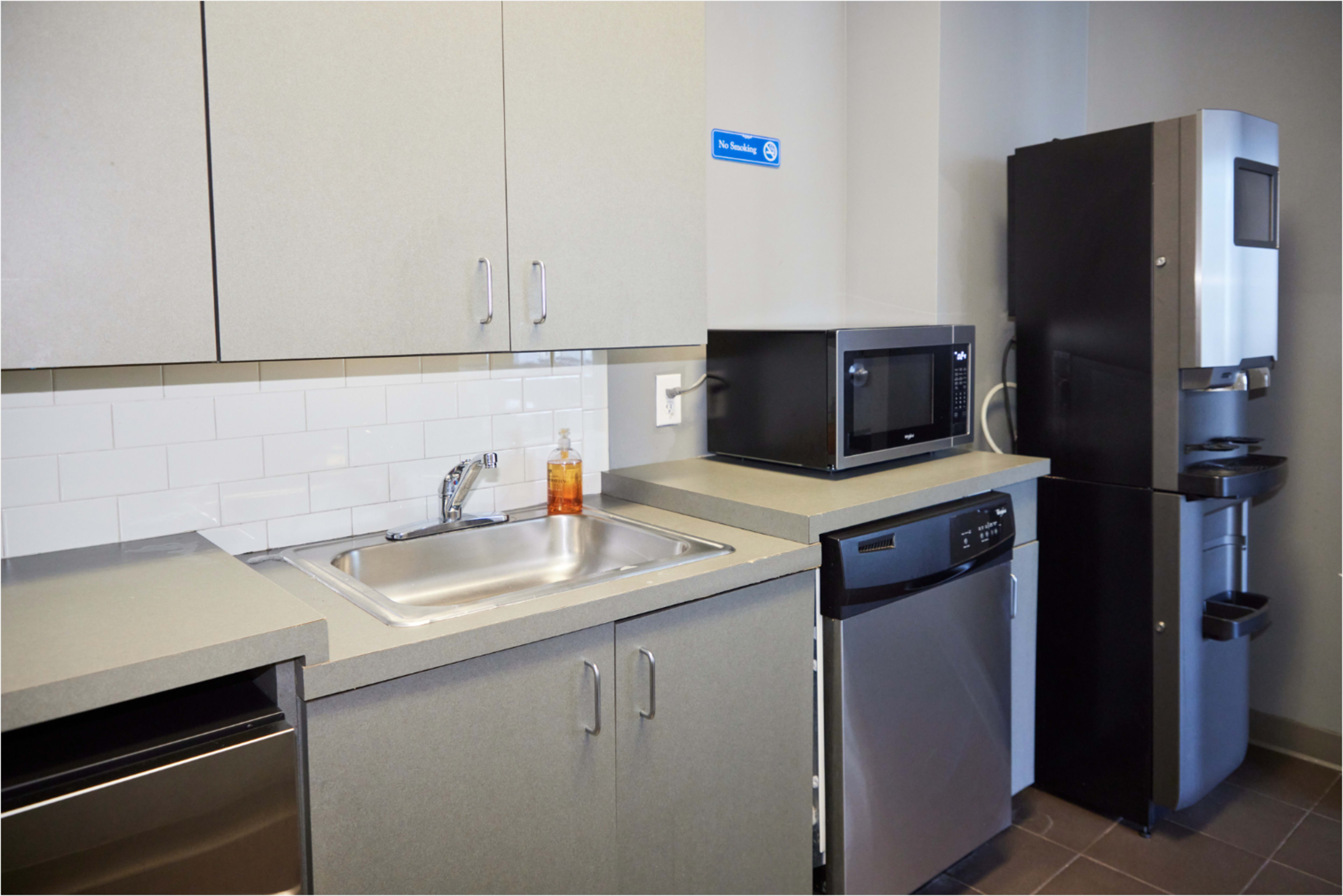 The image shows a modern kitchenette featuring a stainless steel sink, a gray countertop, a microwave, a black refrigerator, and a dishwasher.