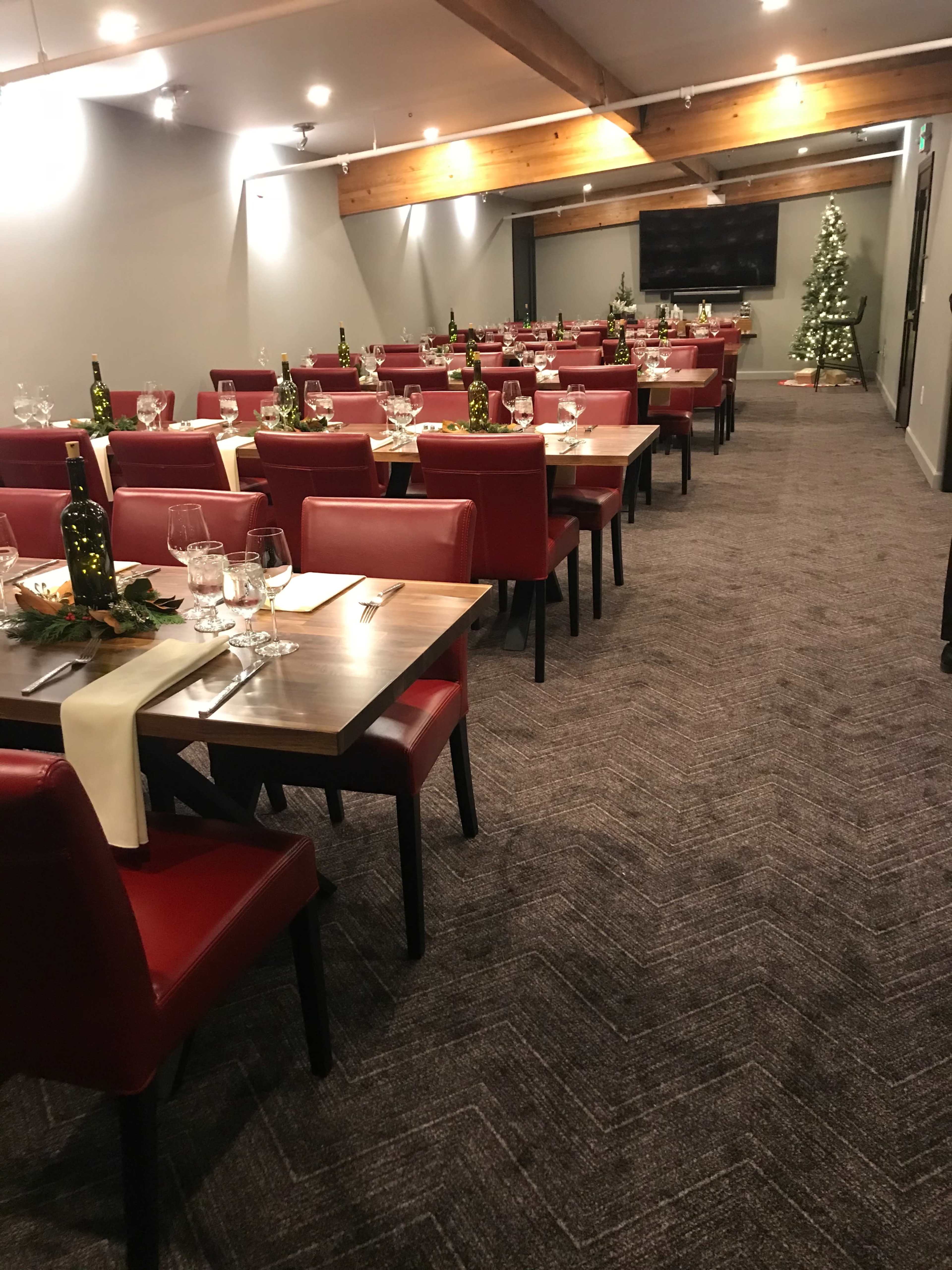 A restaurant dining area features rows of red chairs and tables set with glasses and bottles, leading to a decorated Christmas tree in the corner.