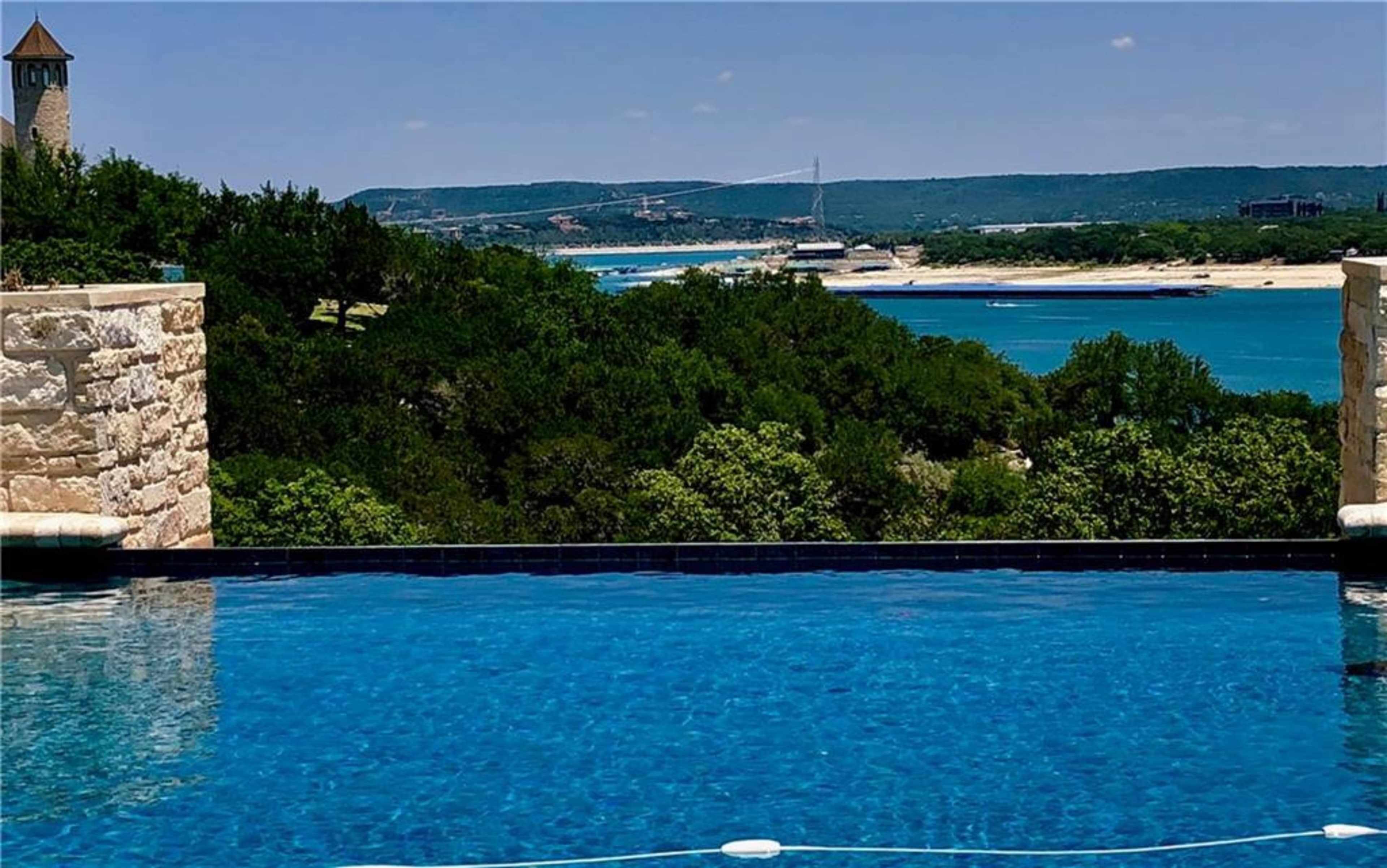 A clear infinity pool with a view of a body of water and green hills in the background.