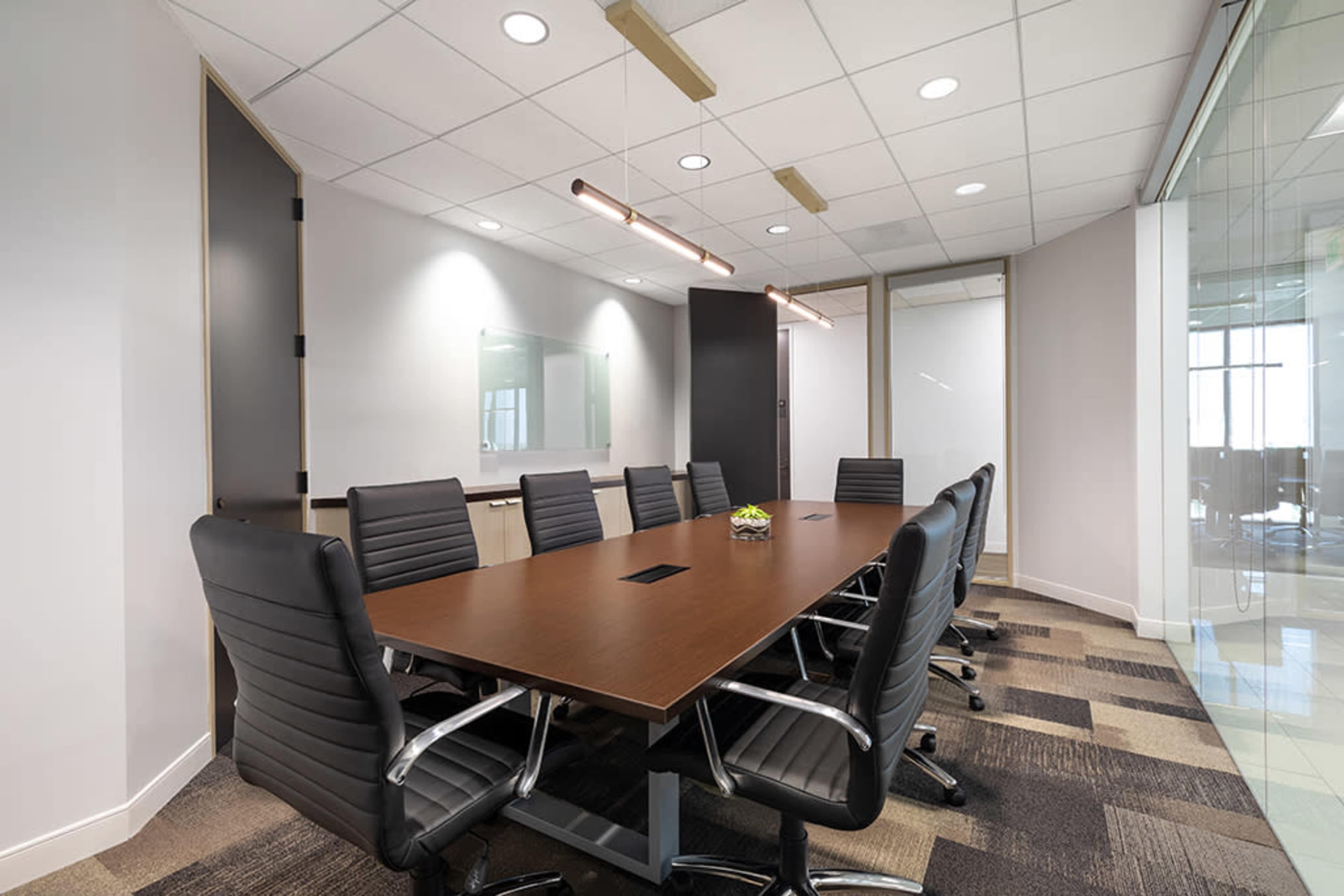 A long conference table is set with black leather chairs in a modern office meeting room.