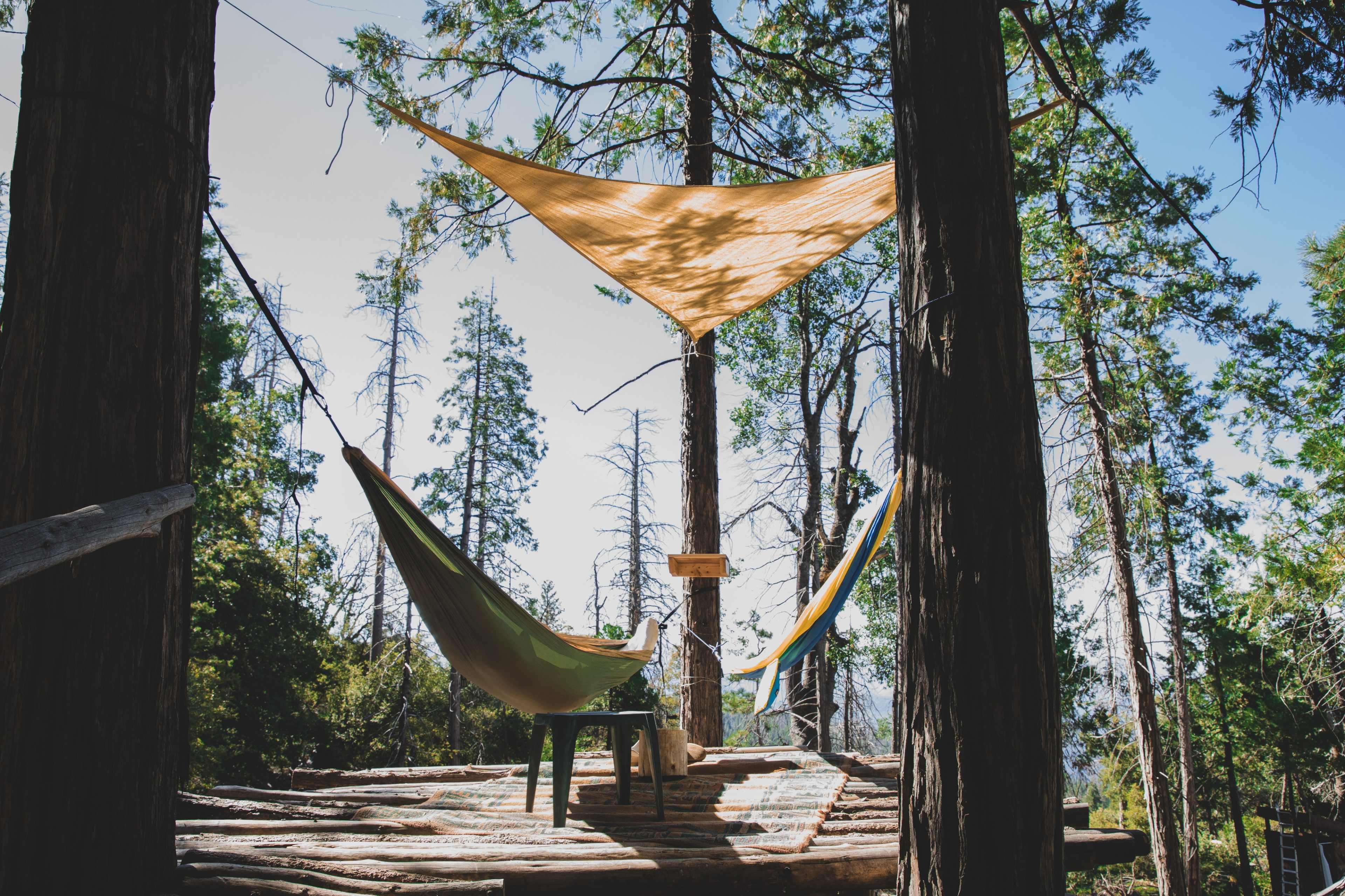 A treehouse platform in a forest, featuring two hammocks suspended between trees and a chair set on the wooden deck.