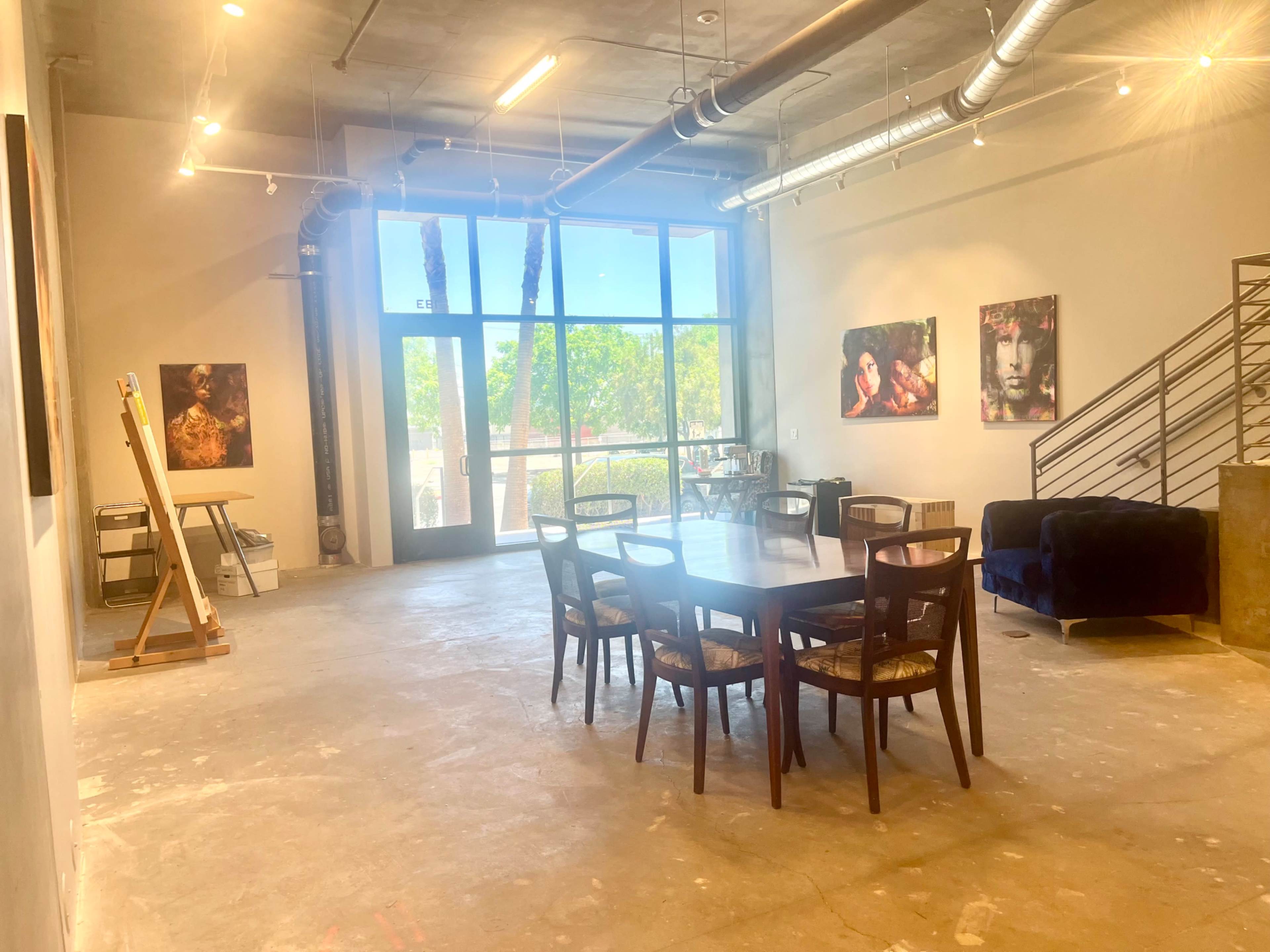 An airy, open space with a dining table surrounded by chairs, artwork on the walls, and large windows letting in natural light.