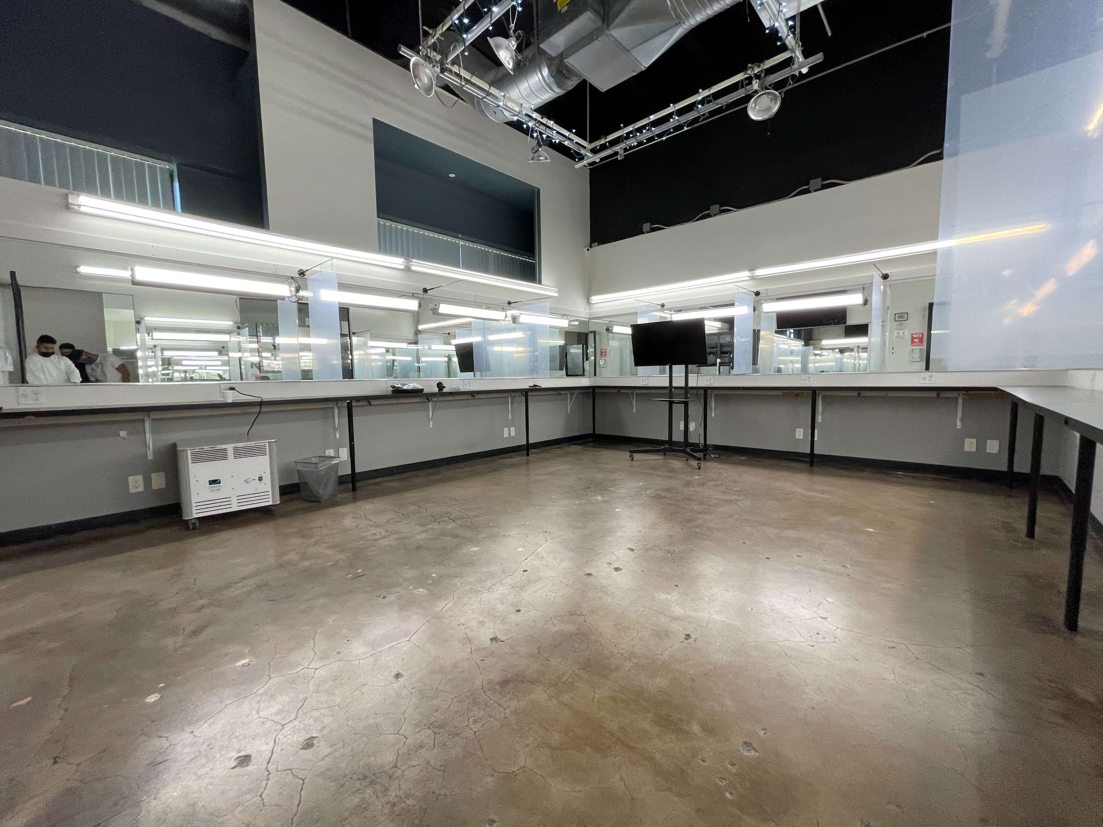 The image shows an empty, well-lit studio space with large mirrors and long worktables against the walls.