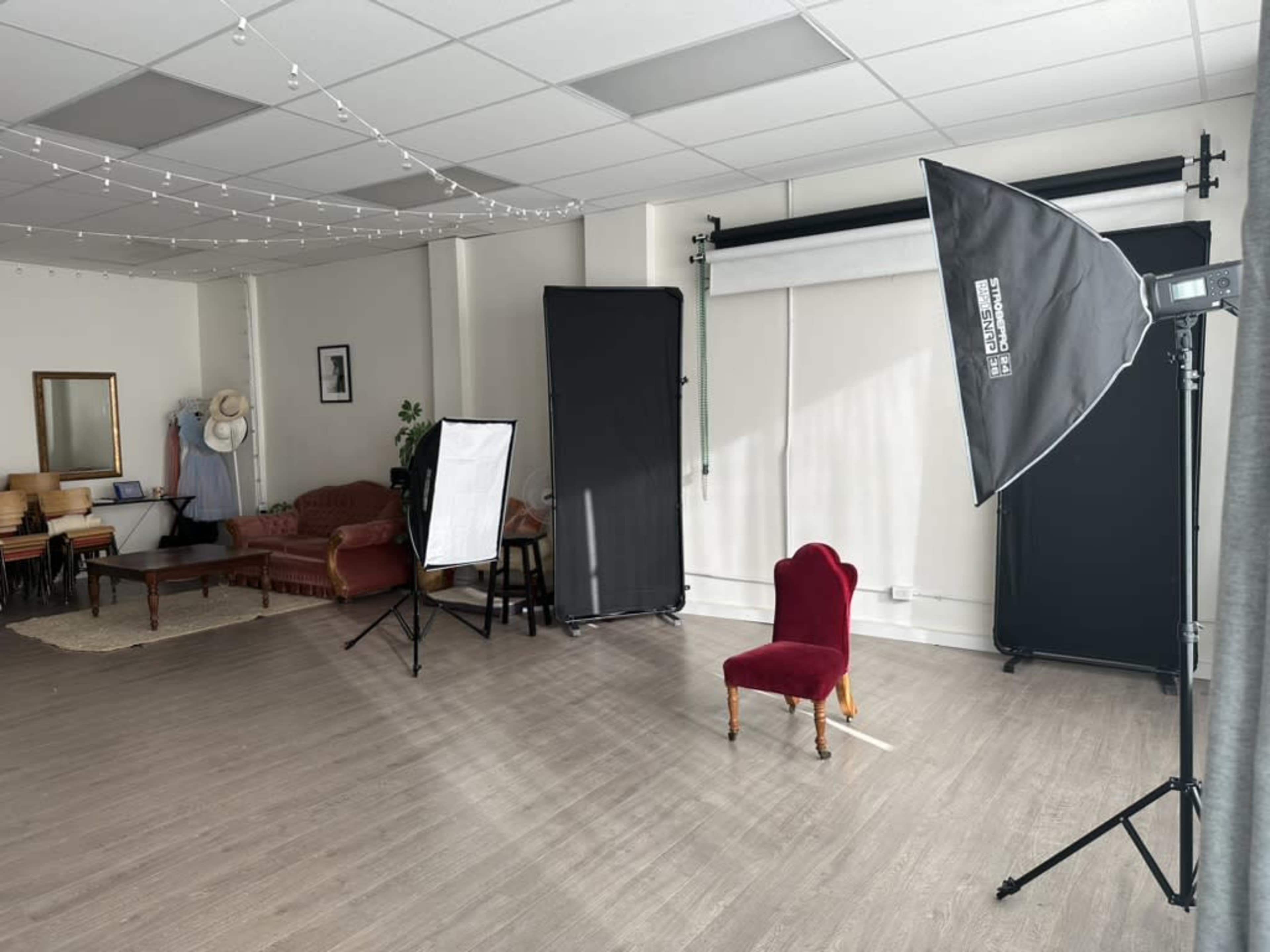 A studio space with a red chair, photography lighting equipment, and backdrops set up for a photoshoot.