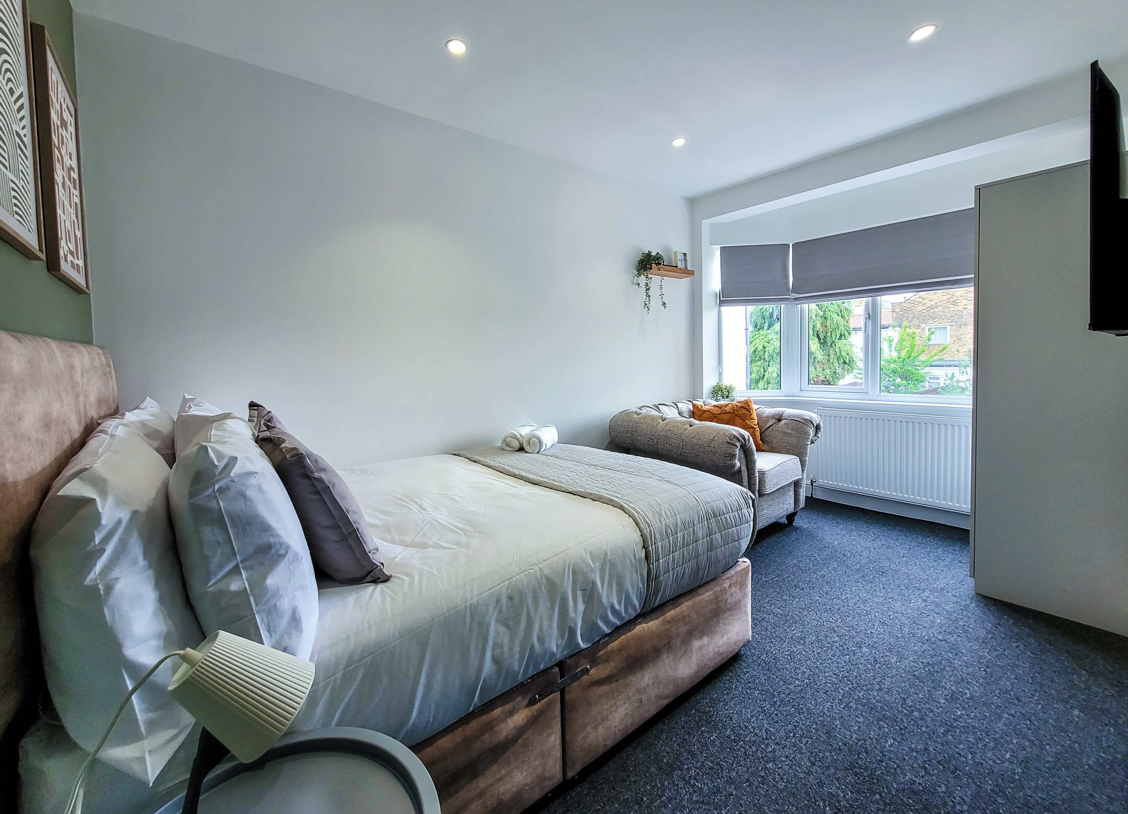A well-lit bedroom with a double bed, a sofa, and a window overlooking greenery outside.