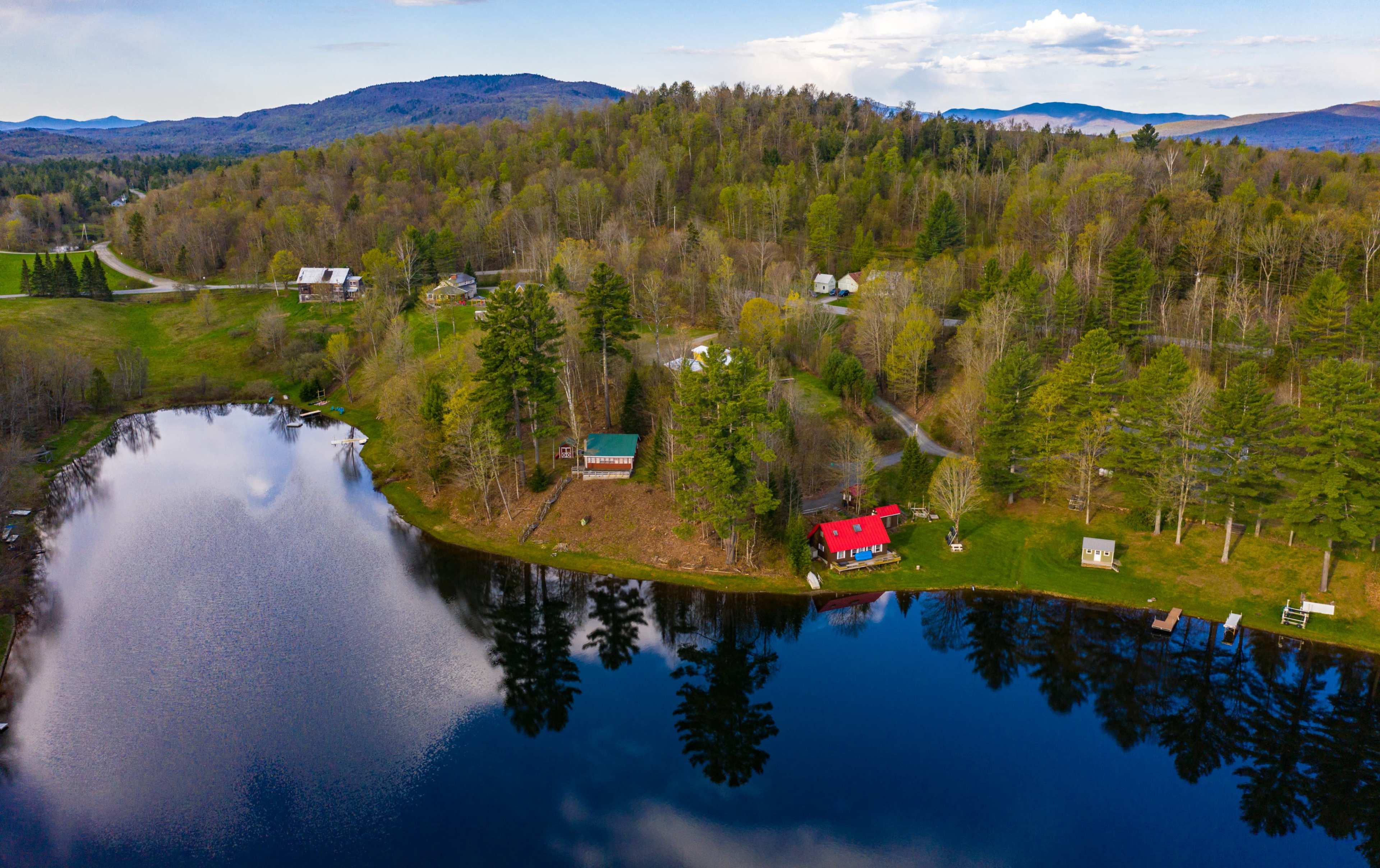 A tranquil lake surrounded by lush greenery and a cluster of houses, with a red-roofed cabin on the shore.