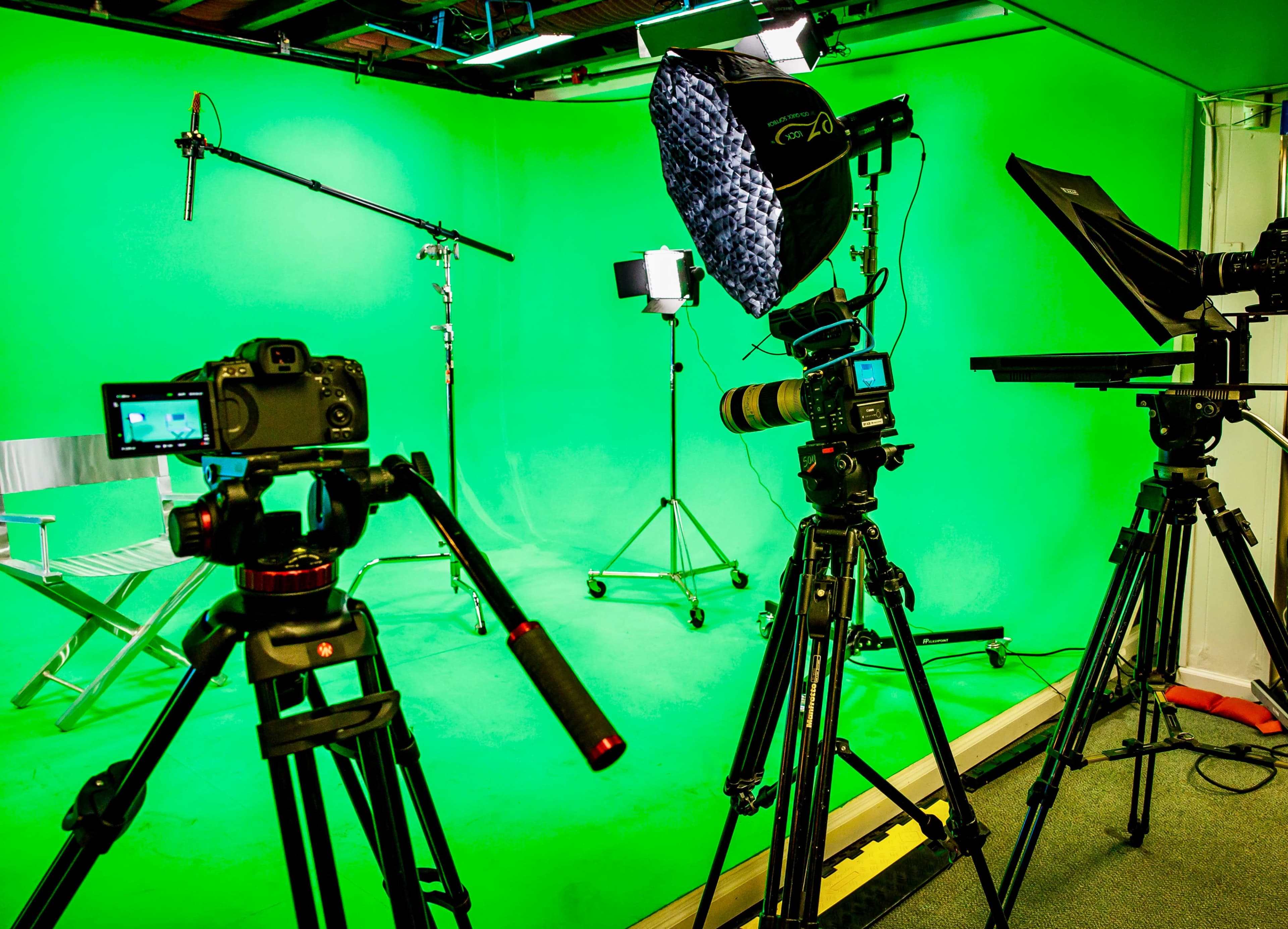 A green screen studio setup with cameras, lighting equipment, and tripods arranged in the space.