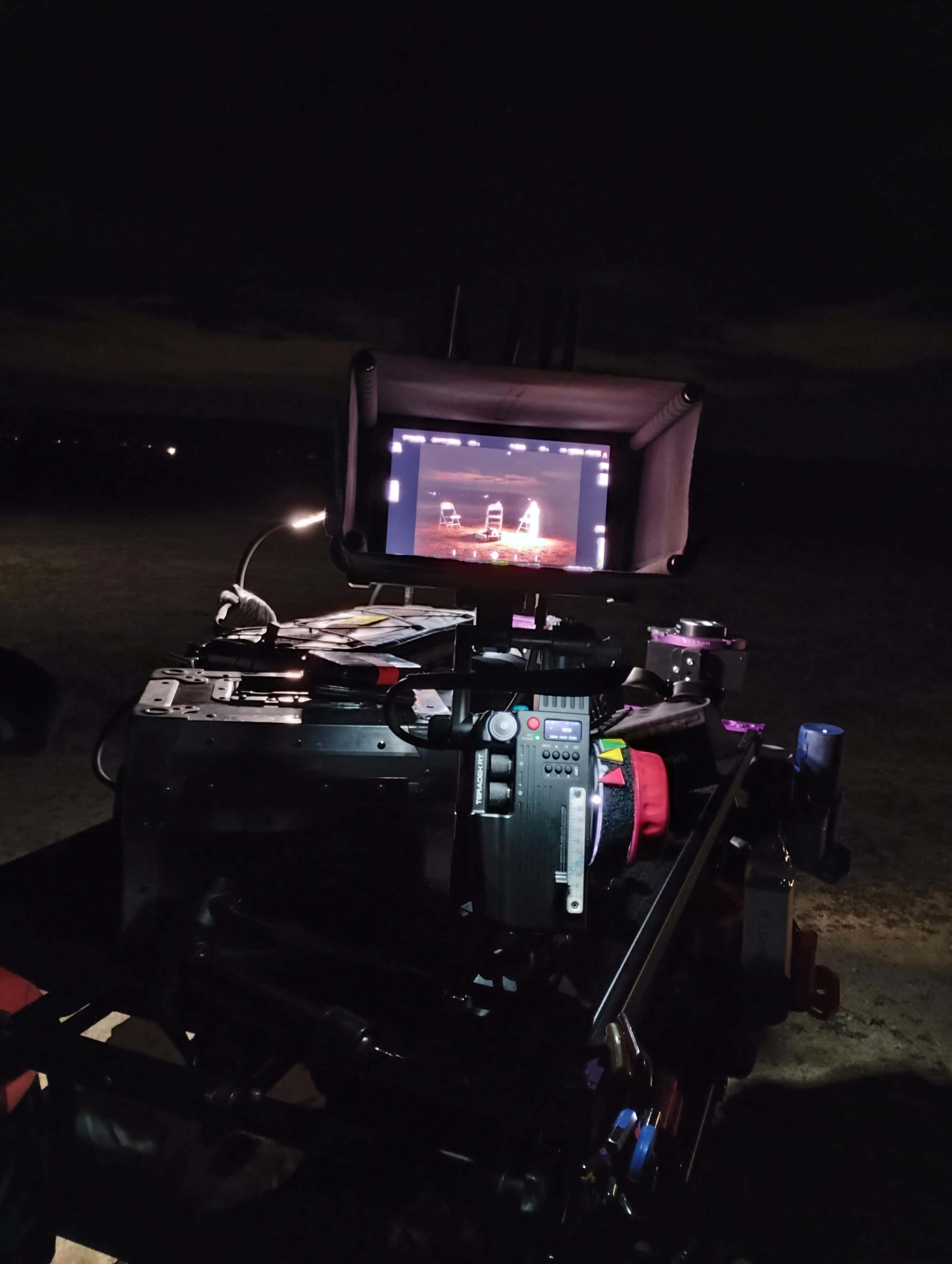 A camera setup is displayed with a monitor showing a live feed, set against a dark, open landscape at night.
