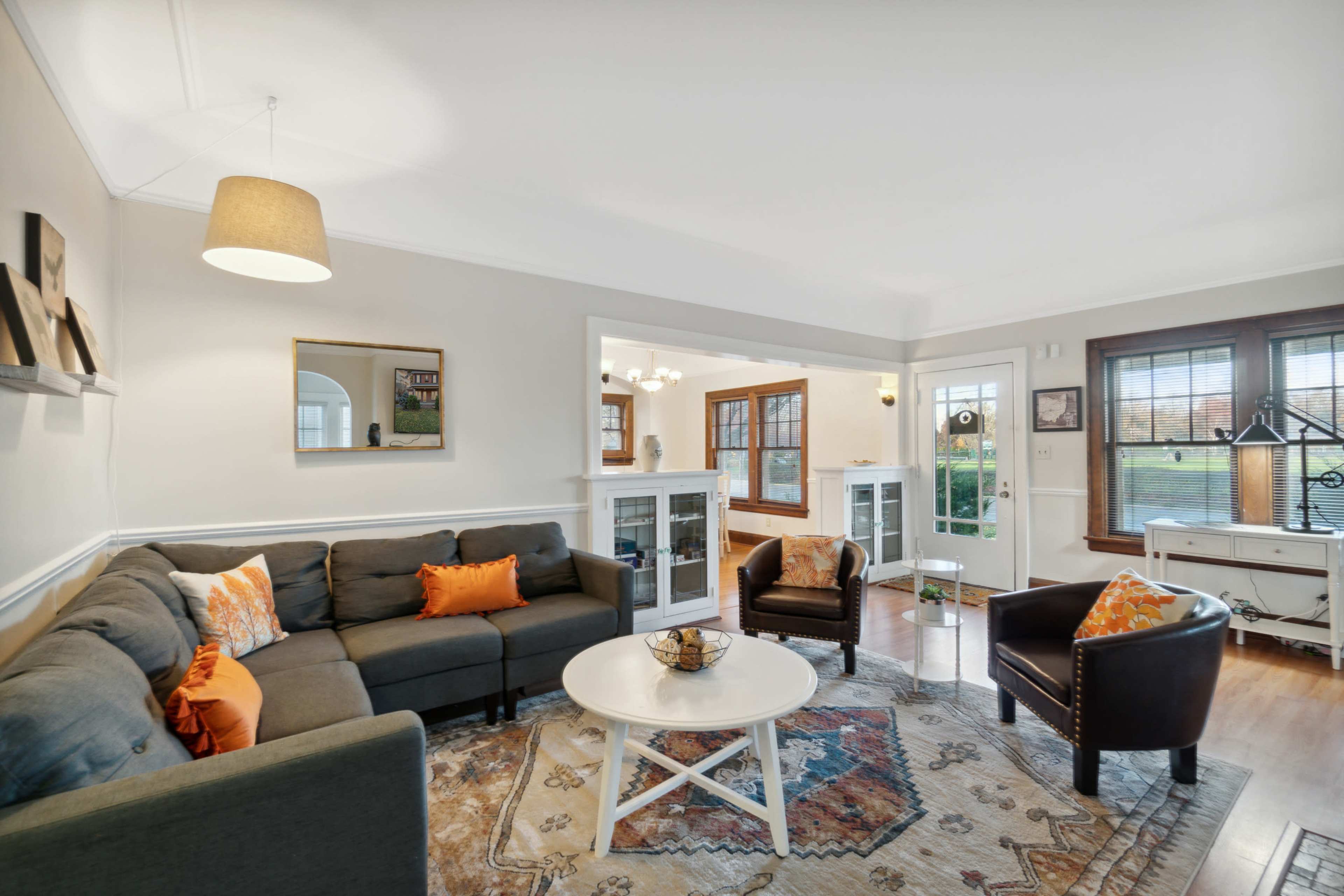 A living room with a gray sectional sofa, a round white coffee table, and large windows allowing natural light to illuminate the space.