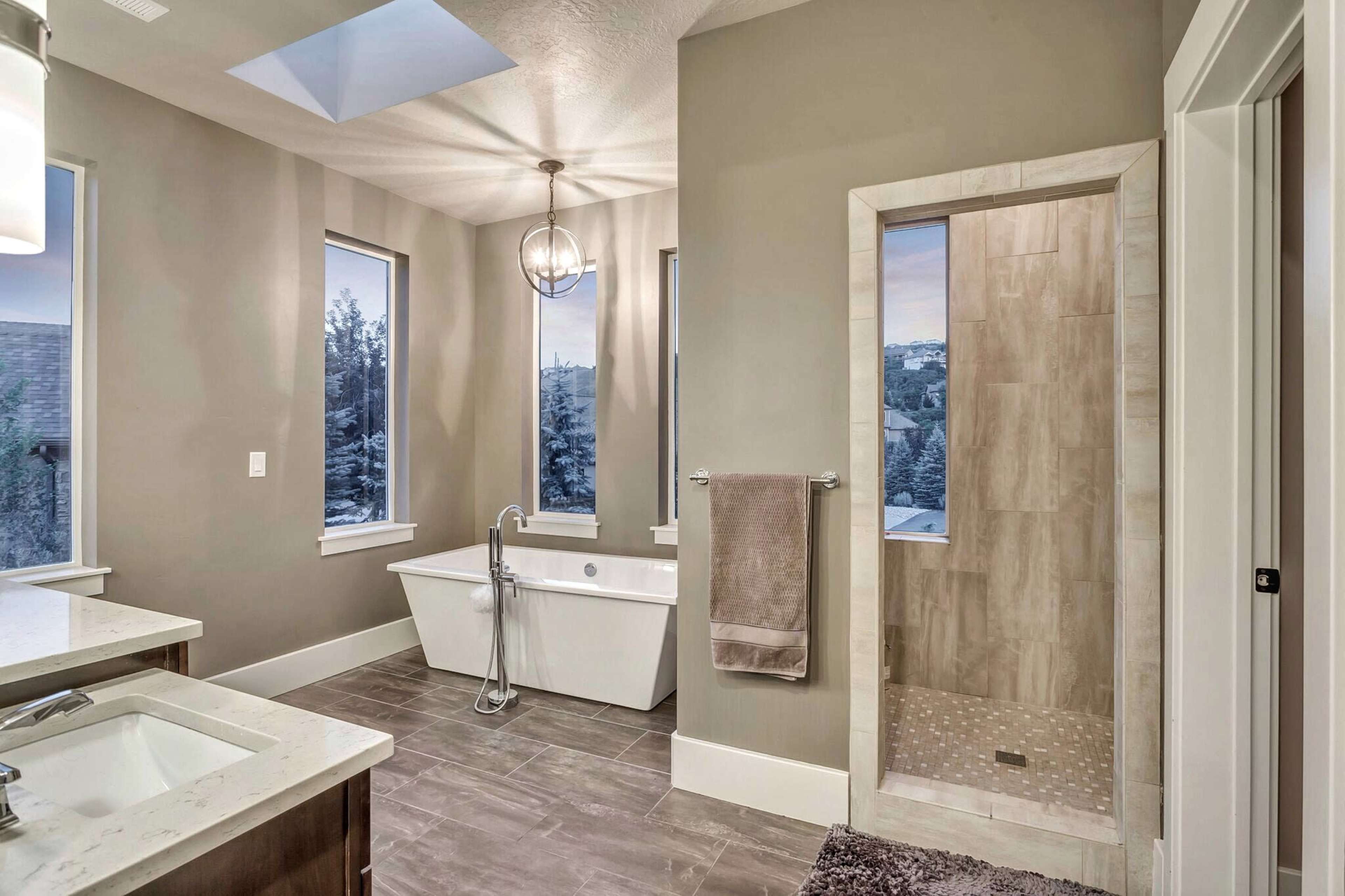 A modern bathroom featuring a freestanding bathtub, a glass-enclosed shower, and large windows allowing natural light.