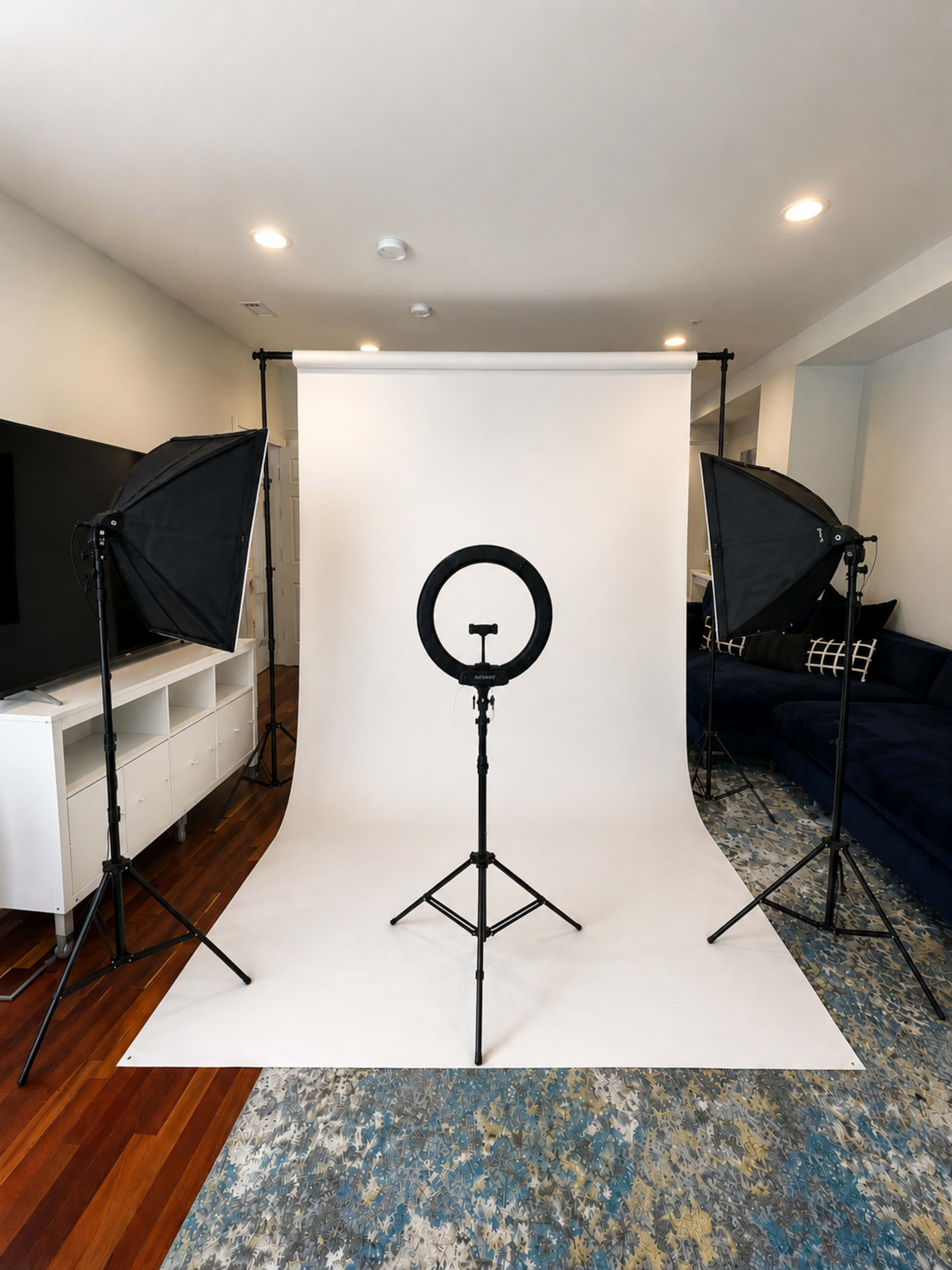 The scene shows a photography setup with a white backdrop and two softbox lights flanking a ring light on a stand.