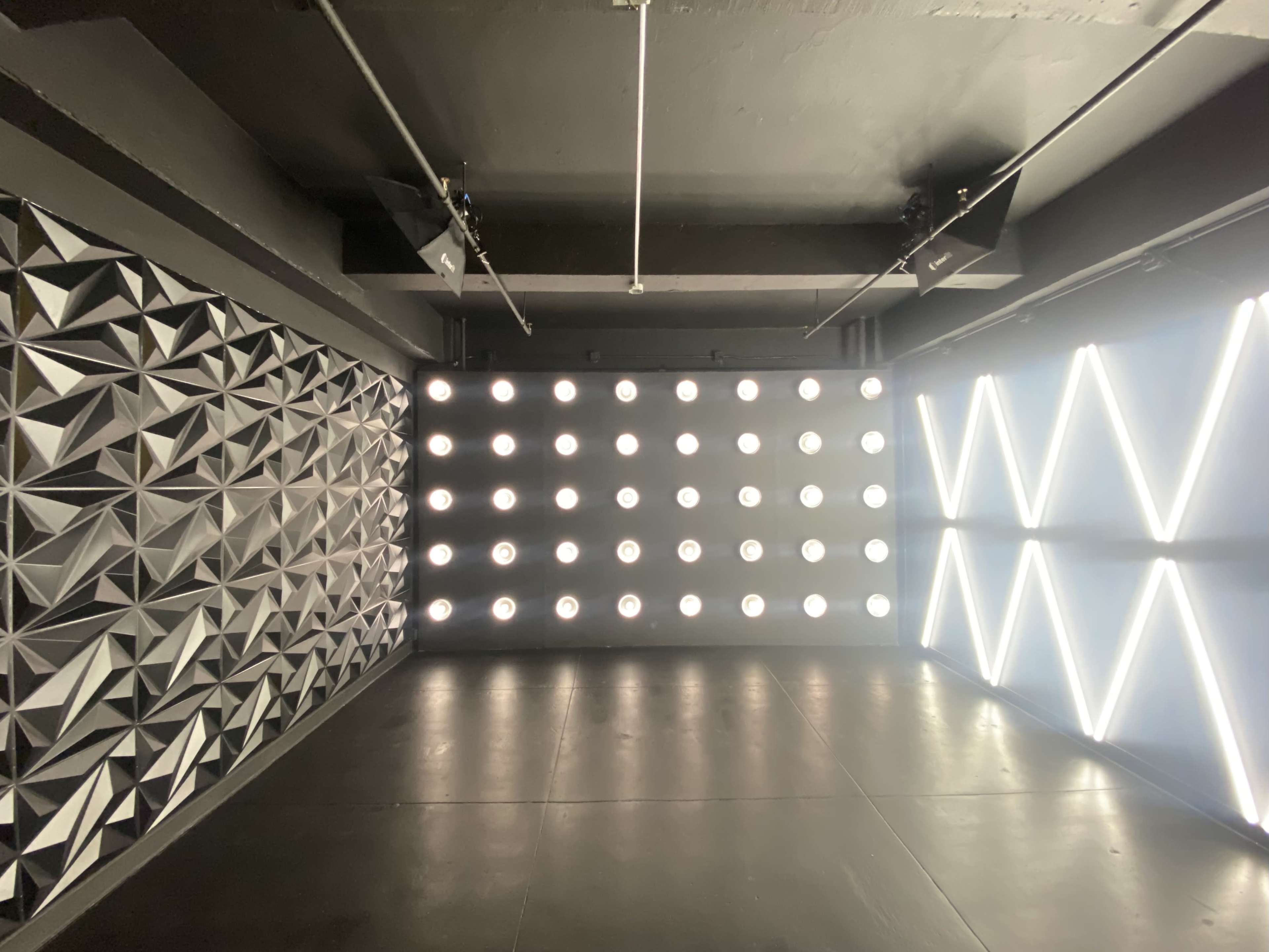 A modern interior space with textured wall panels, a grid of circular lights on one wall, and diagonal line lights on another.