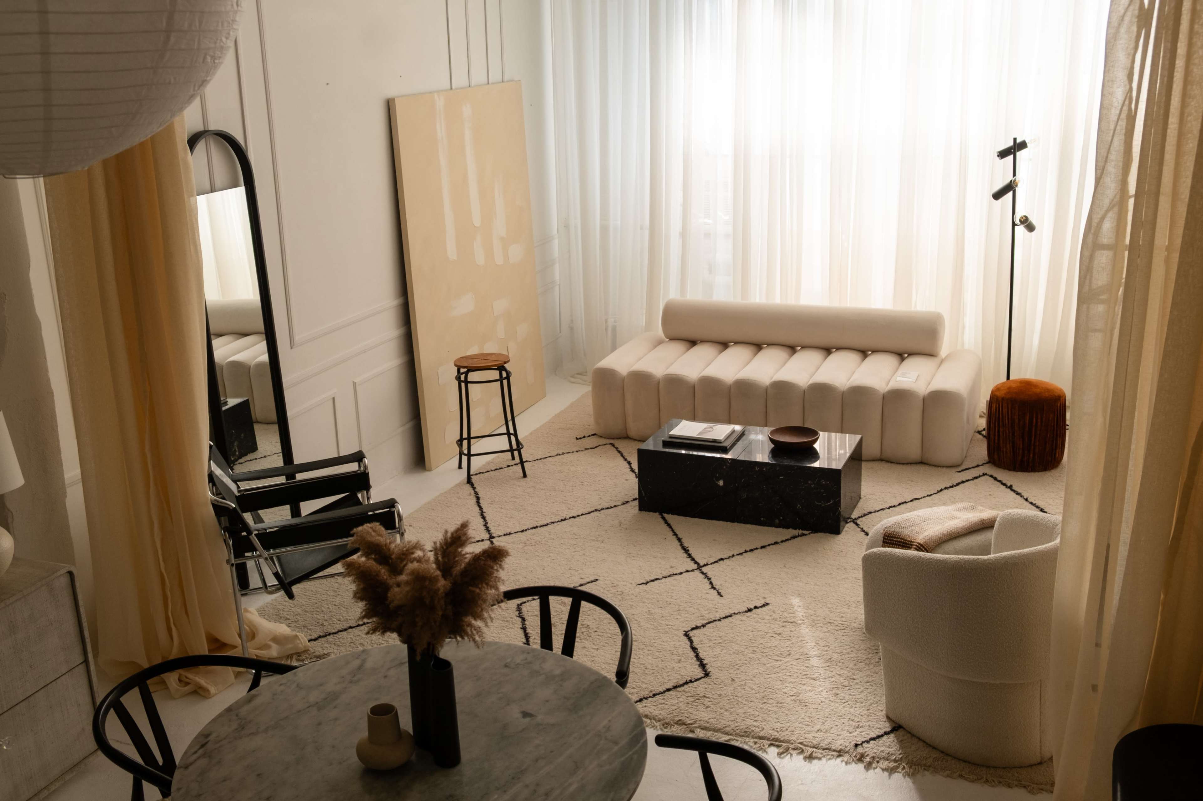 The scene features a modern, stylish living room with a light color palette, a plush sofa, and a combination of minimalistic furniture.