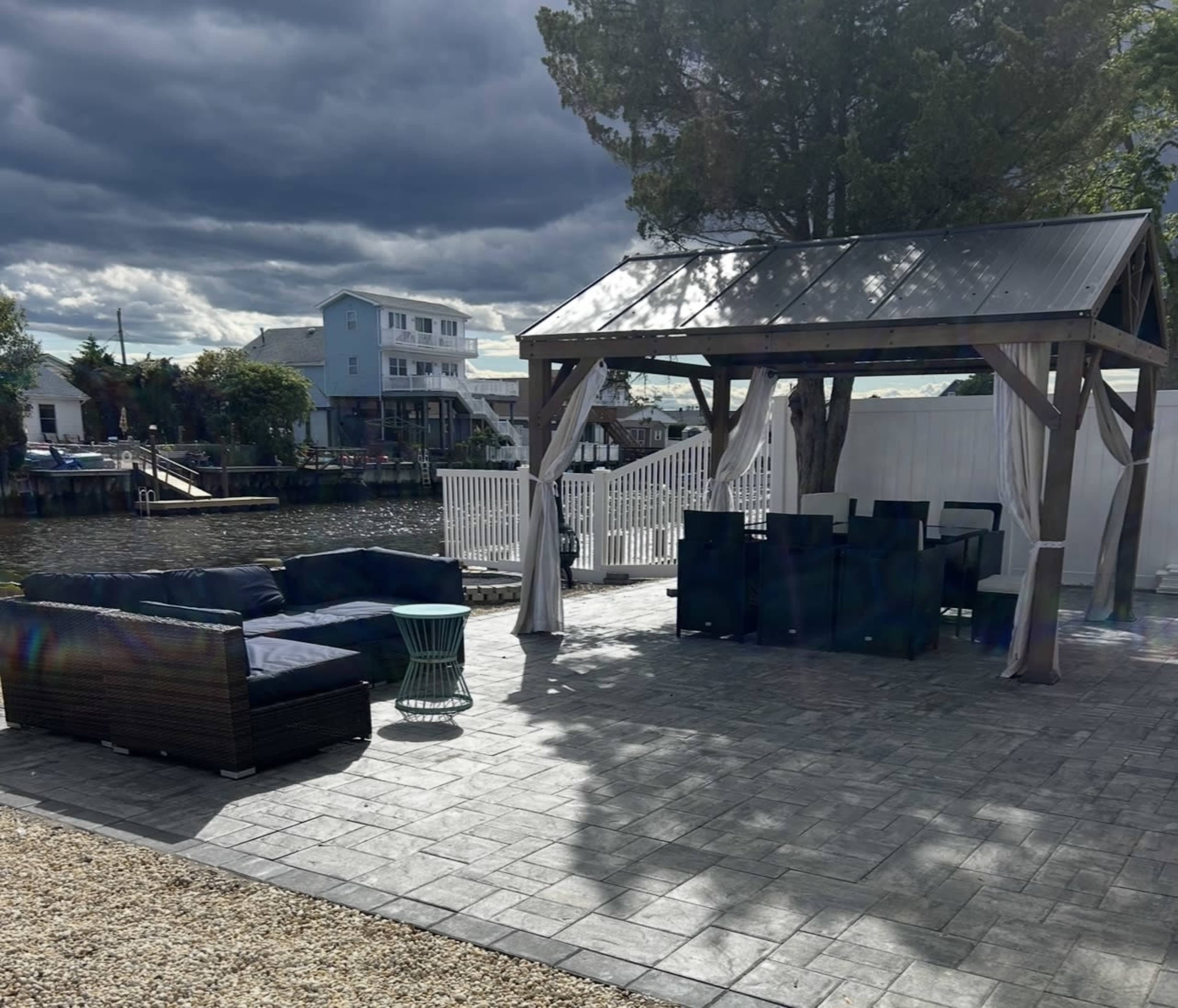 A patio area features a covered gazebo with seating and a dining set, adjacent to a canal with a cloudy sky overhead.