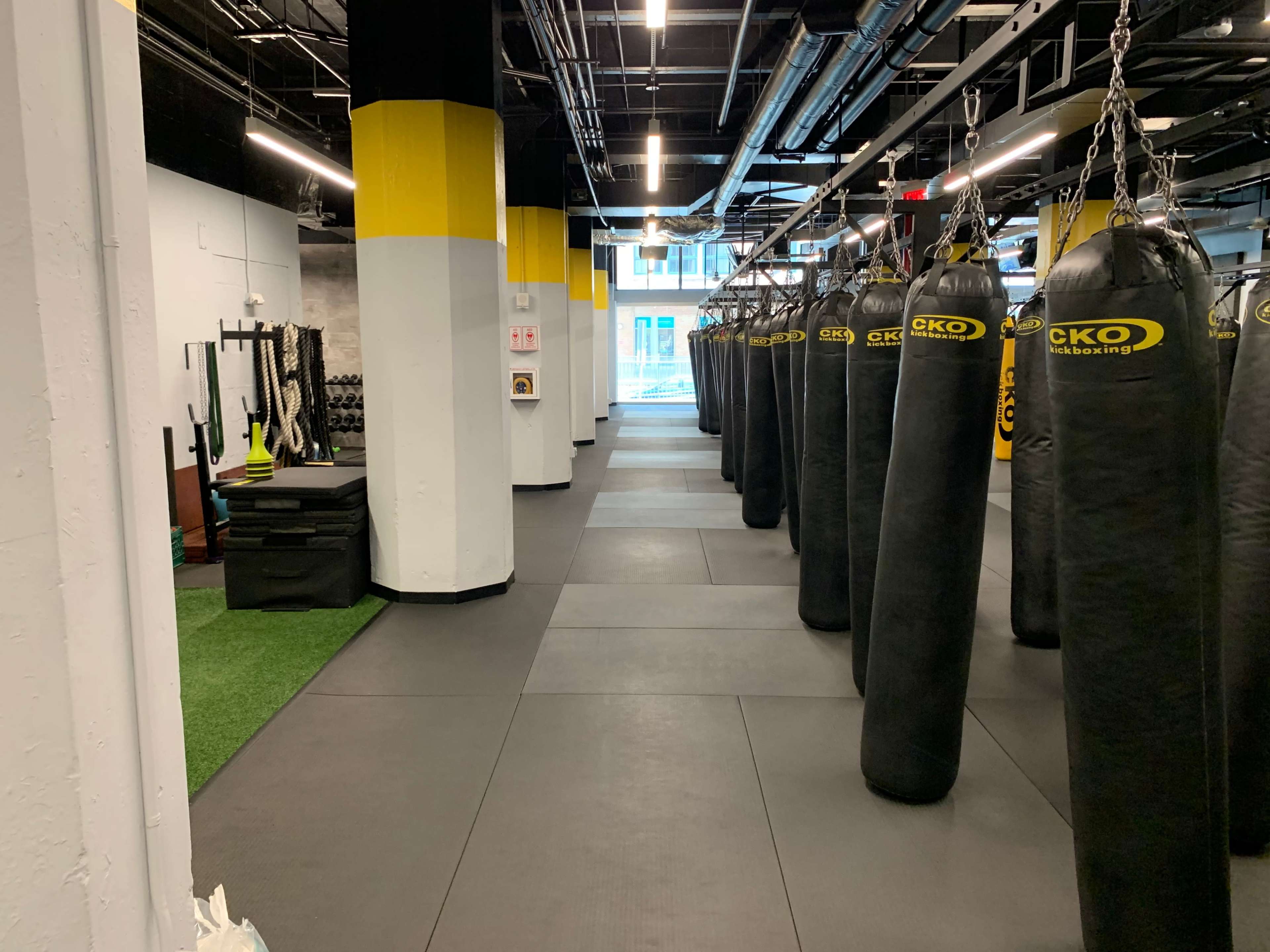 A fitness facility with rows of heavy punching bags, a turf area with equipment, and exercise mats.