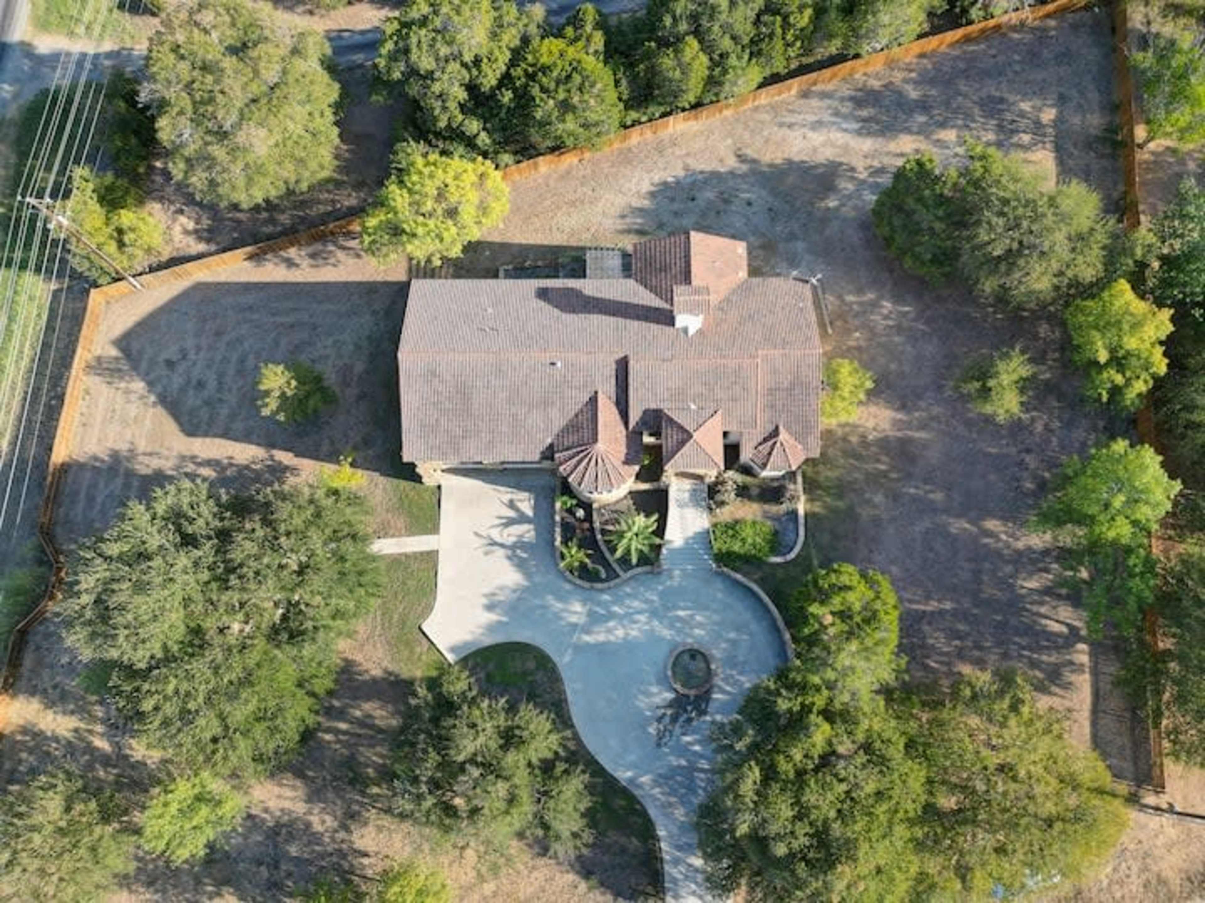 An aerial view shows a house with a tiled roof surrounded by a landscaped yard and a winding driveway.