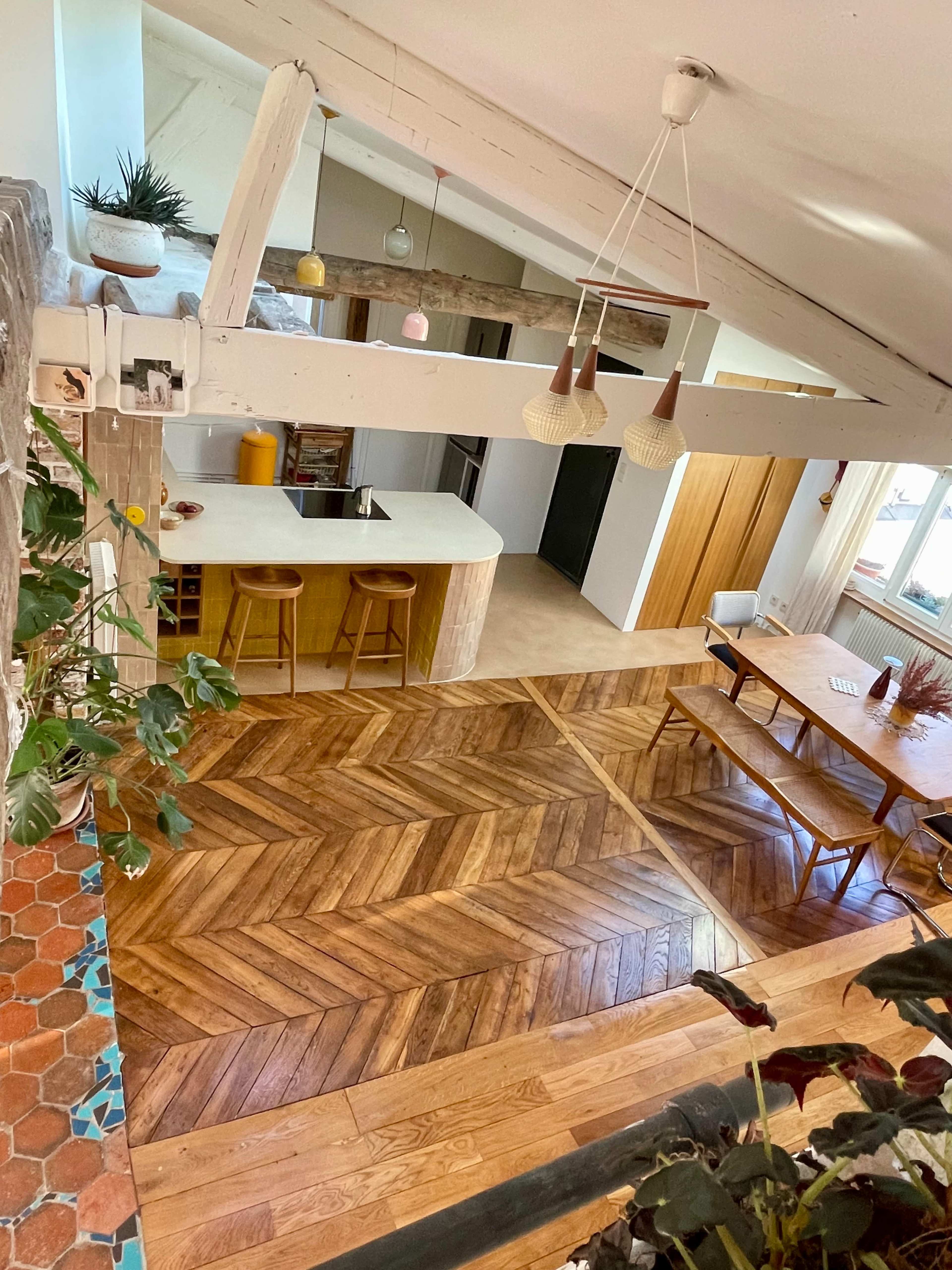 The image shows an open-concept kitchen and dining area with wooden flooring arranged in a herringbone pattern and a large dining table.