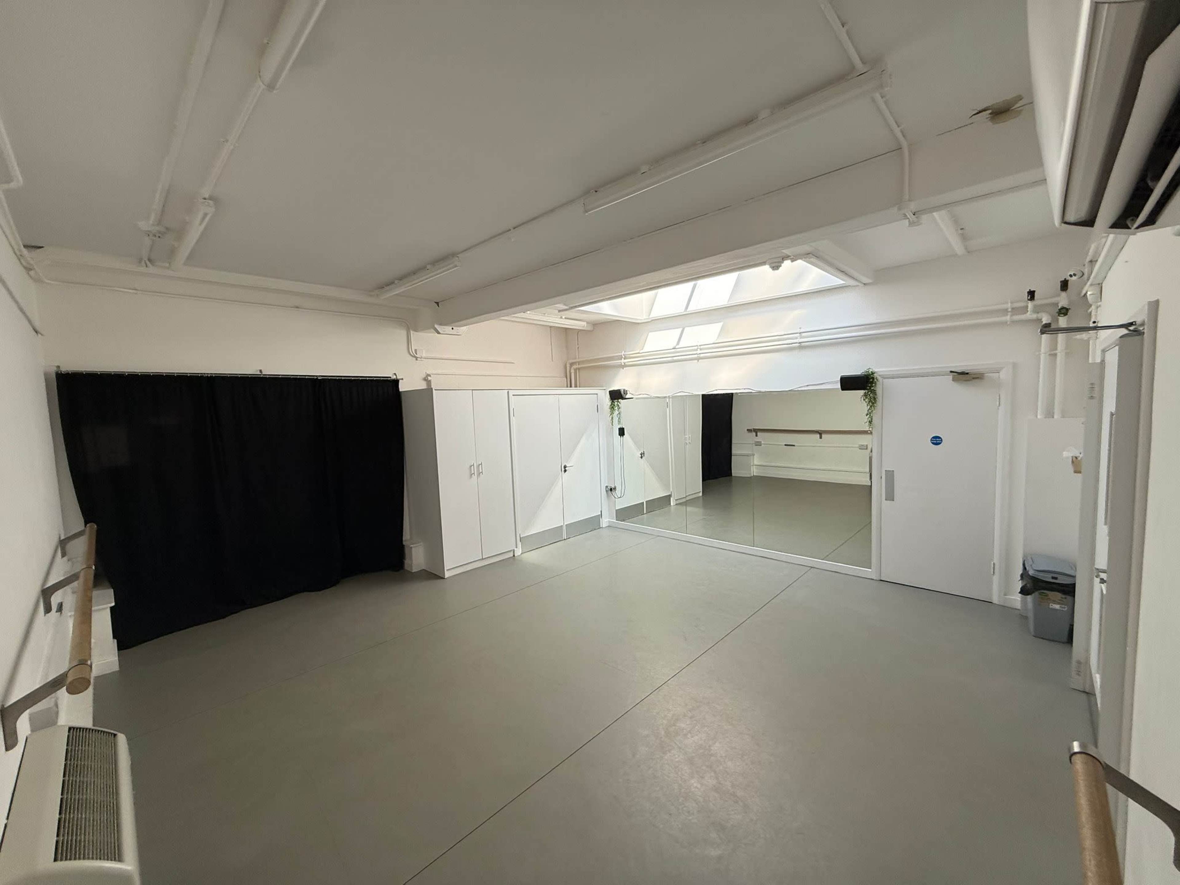The image shows a spacious studio with white walls, a large mirror, and a black curtain section dividing the space.