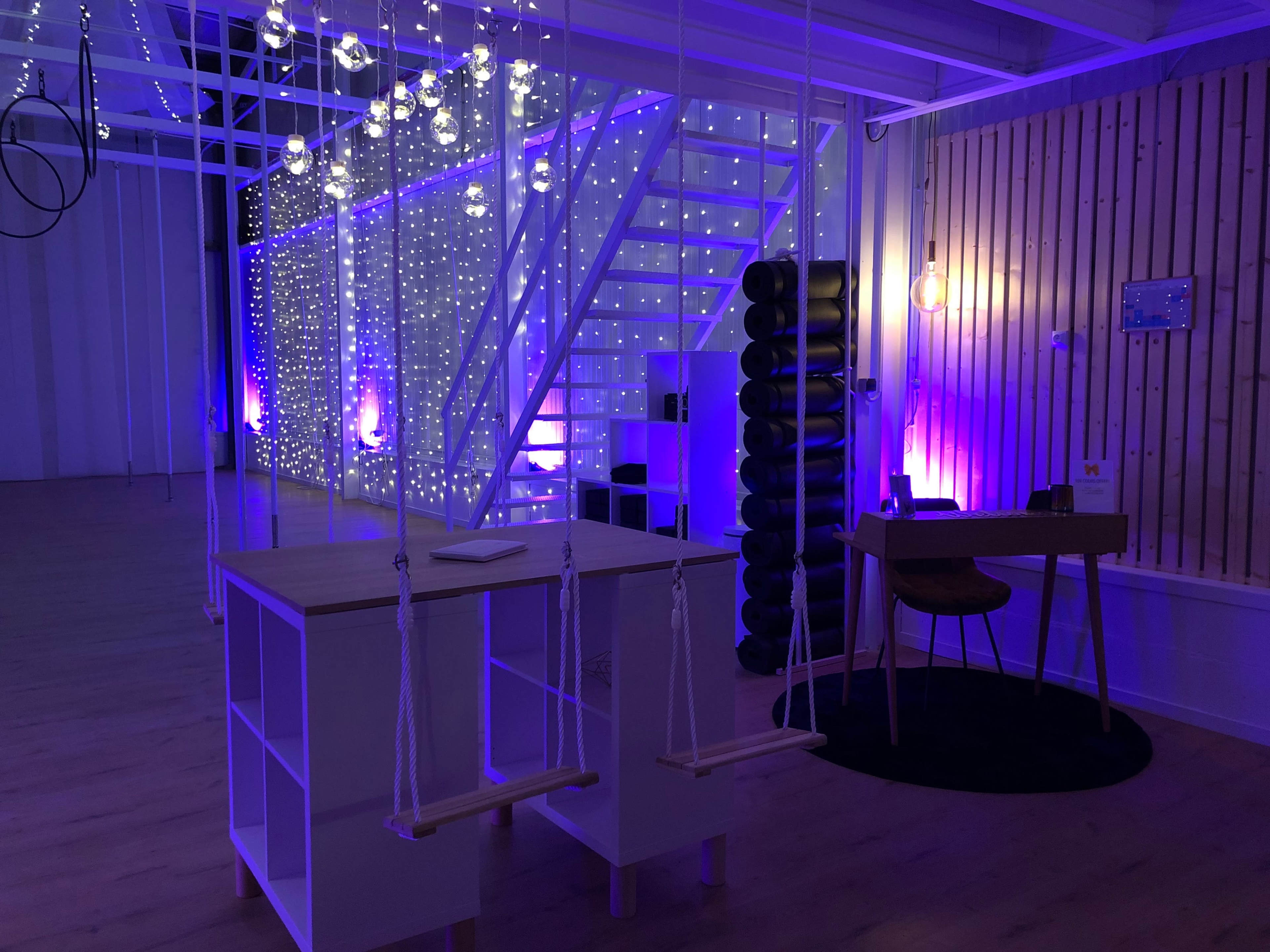 A modern interior space featuring a staircase, illuminated walls with string lights, and a table with swings attached.